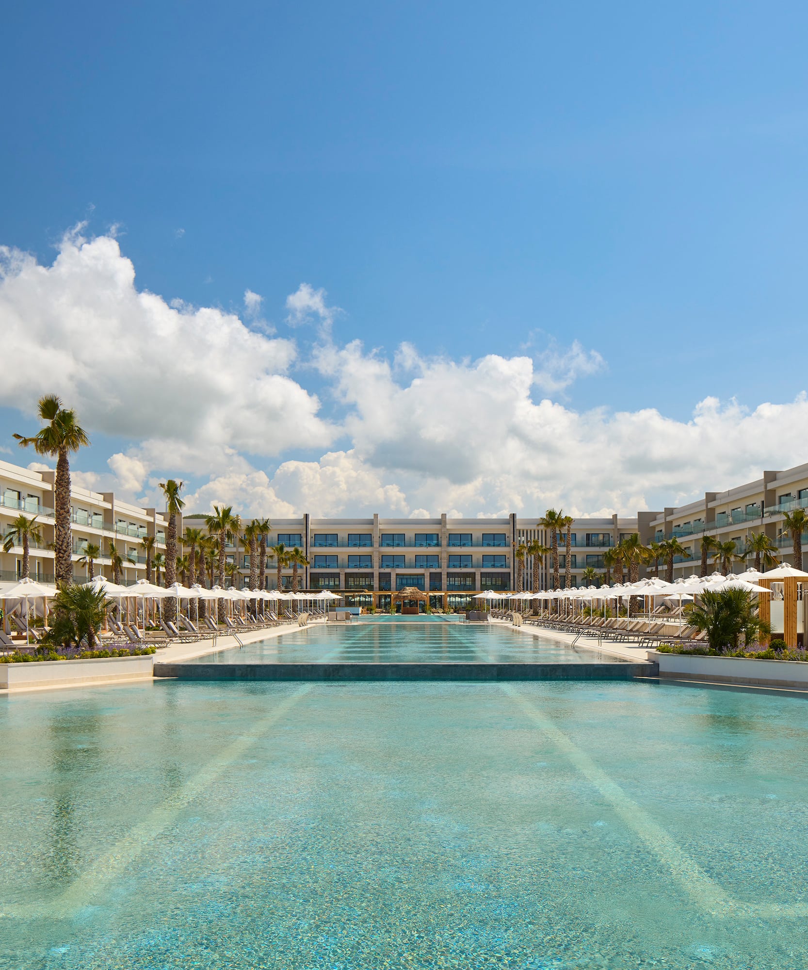 a pool with umbrellas and palm trees in front of a hotel