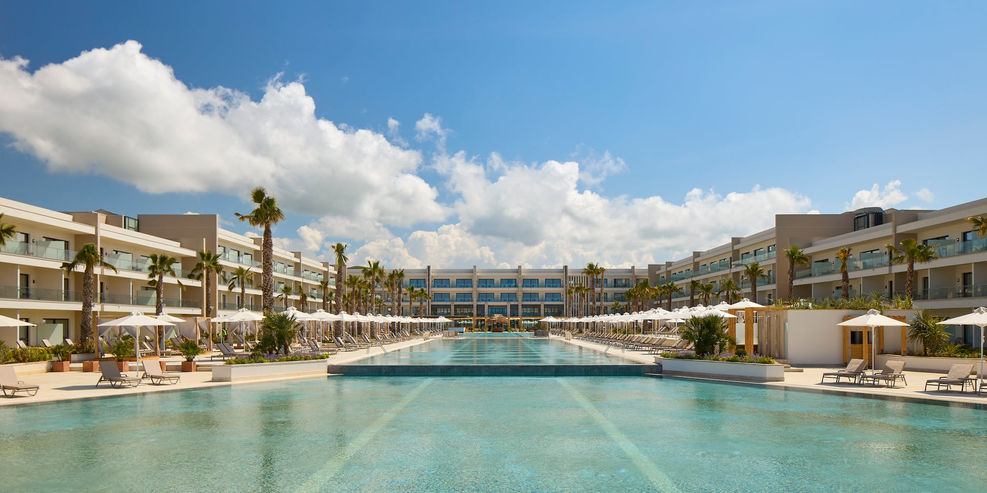 a pool with umbrellas and palm trees in front of a hotel