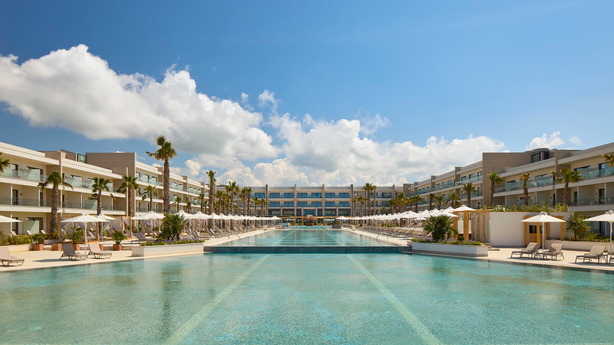 a pool with umbrellas and palm trees in front of a hotel