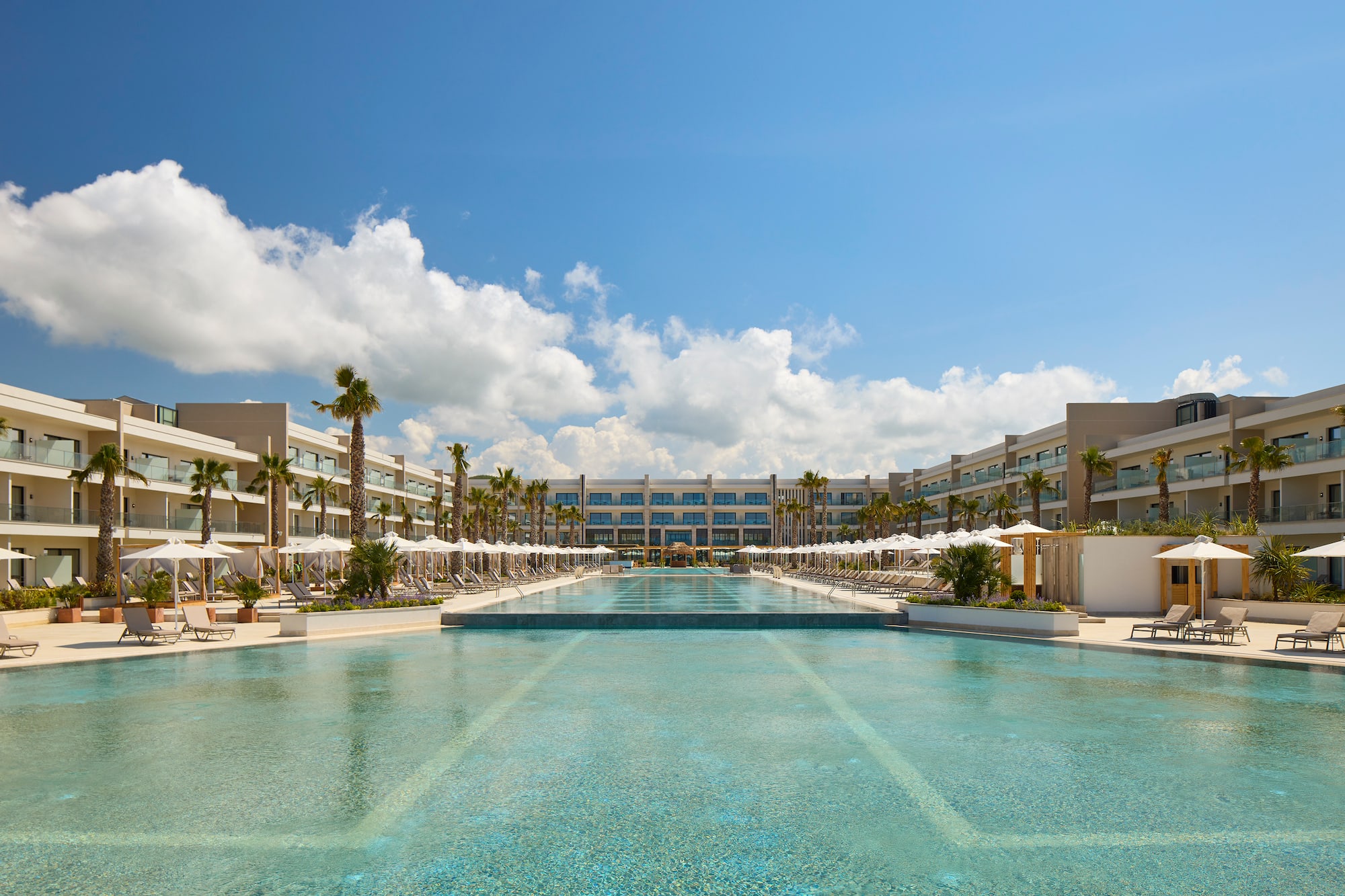 a pool with umbrellas and palm trees in front of a hotel