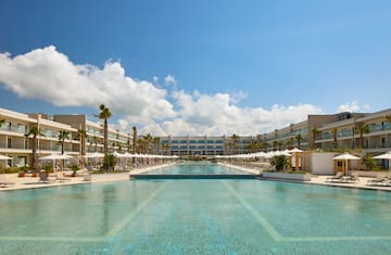 a pool with umbrellas and palm trees in front of a hotel
