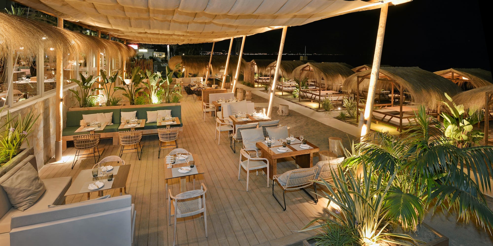 Nighttime beach bar restaurant, elegant outdoor dining area with thatched cabanas.