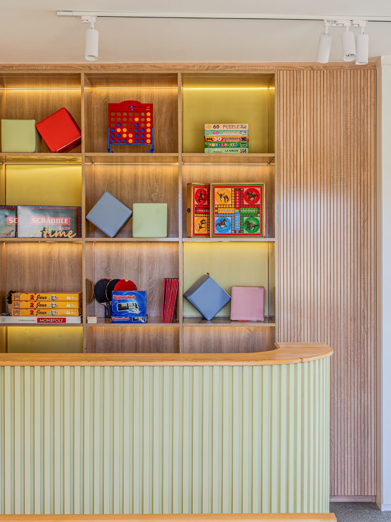Kids Club: mostrador verde, estantería con juegos de mesa y mural colorido.
