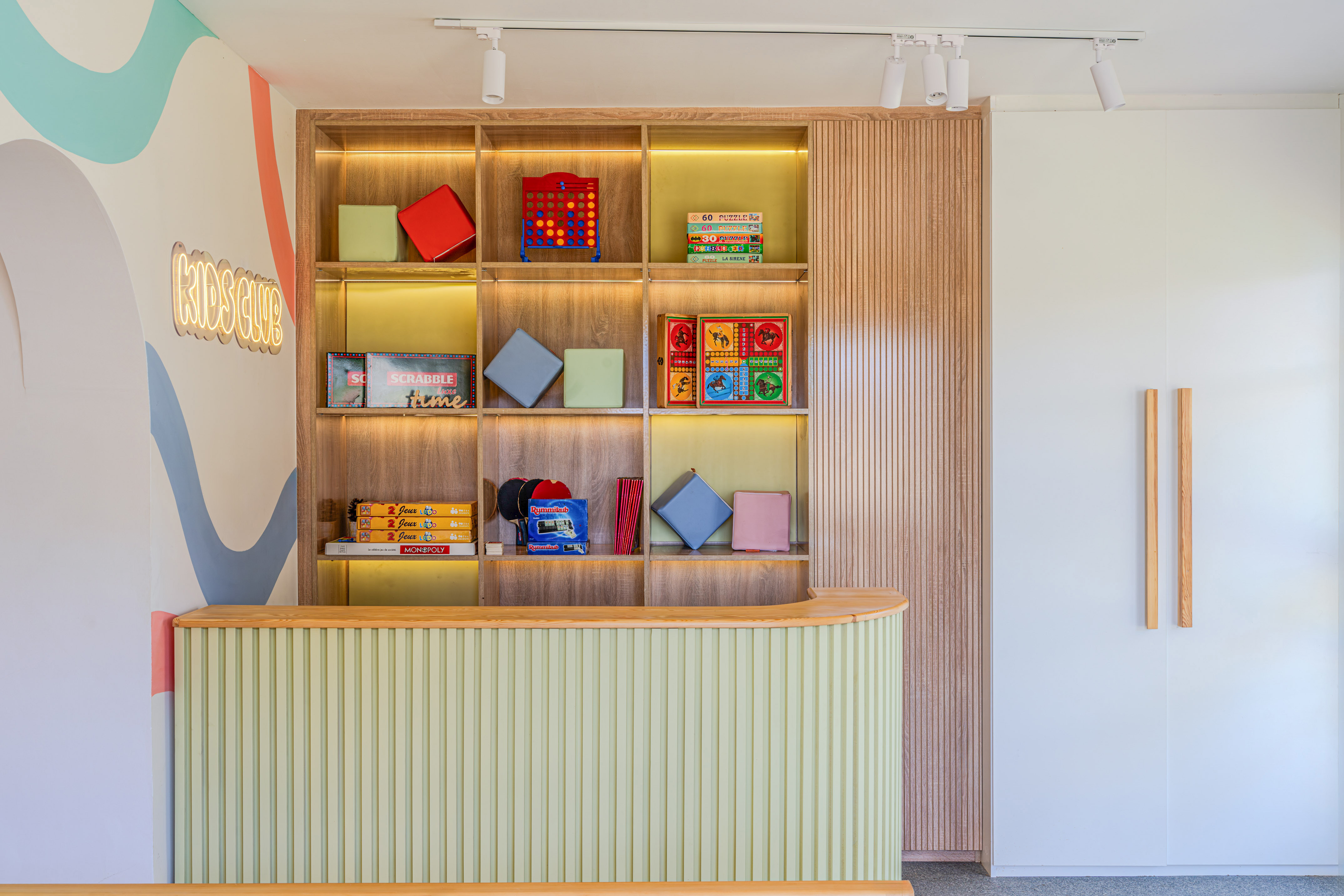 Kids Club: mostrador verde, estantería con juegos de mesa y mural colorido.