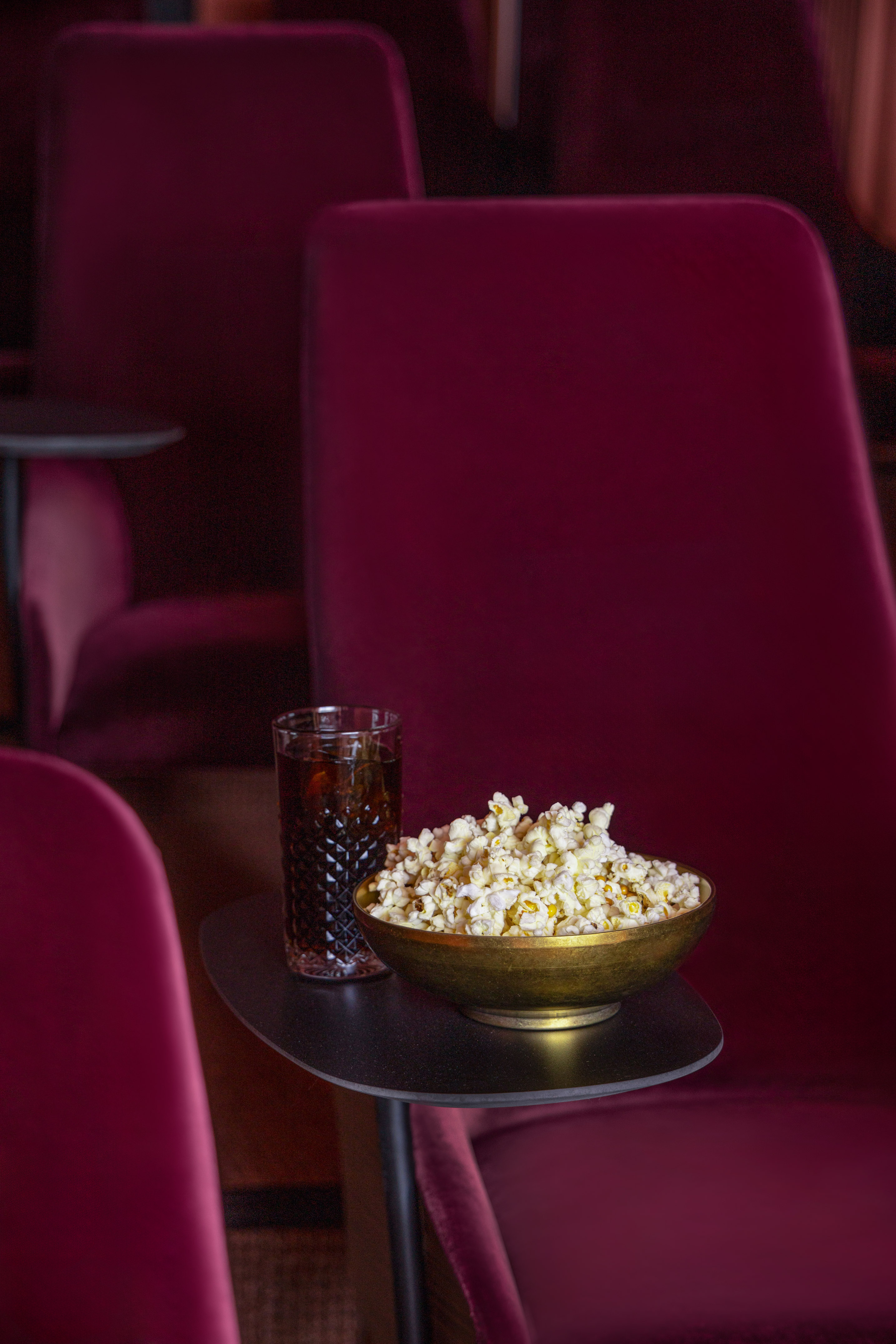 Popcorn and soda in a luxury movie theater with red velvet seats.