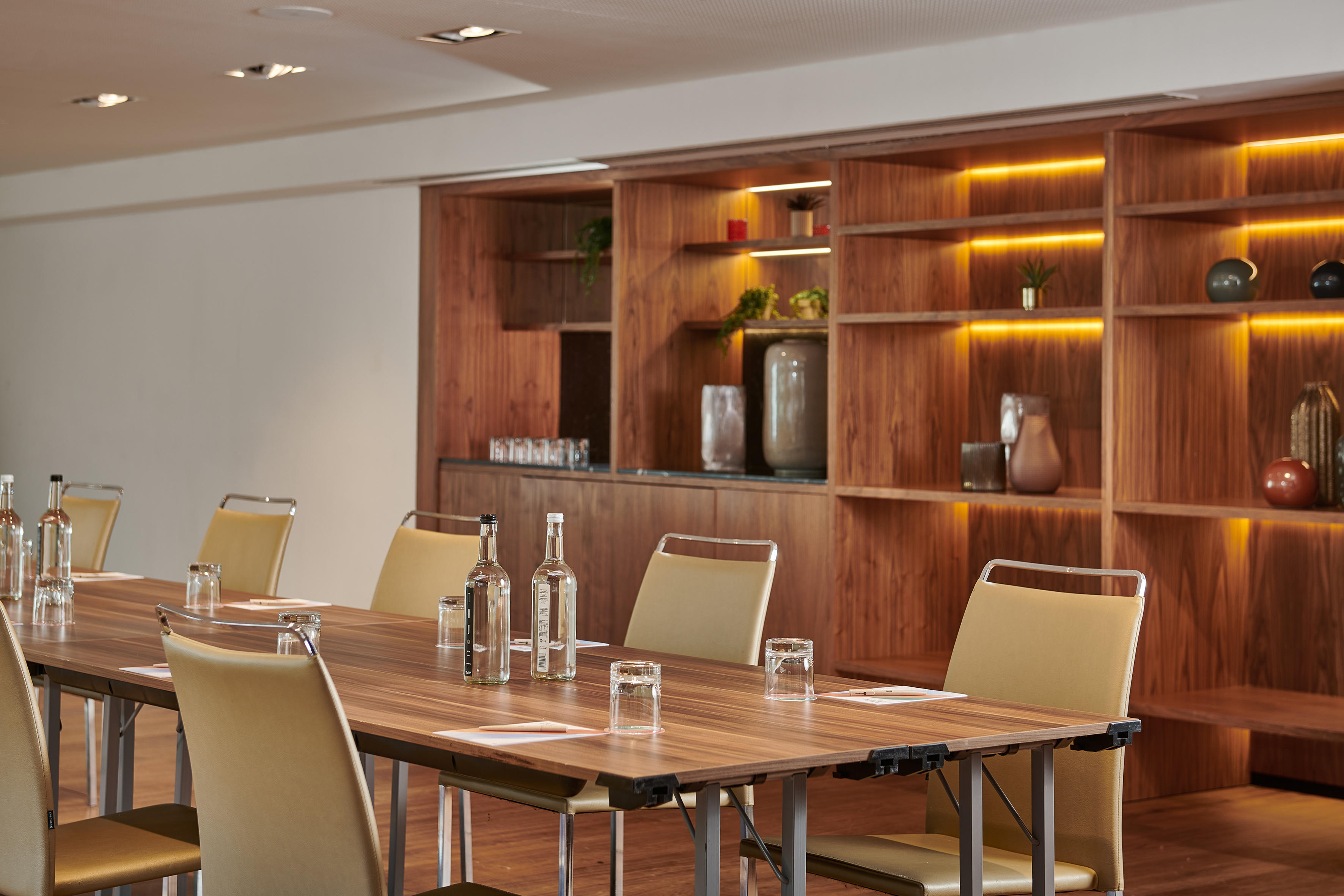 Modern conference room with long wooden table, chairs, and backlit shelves.