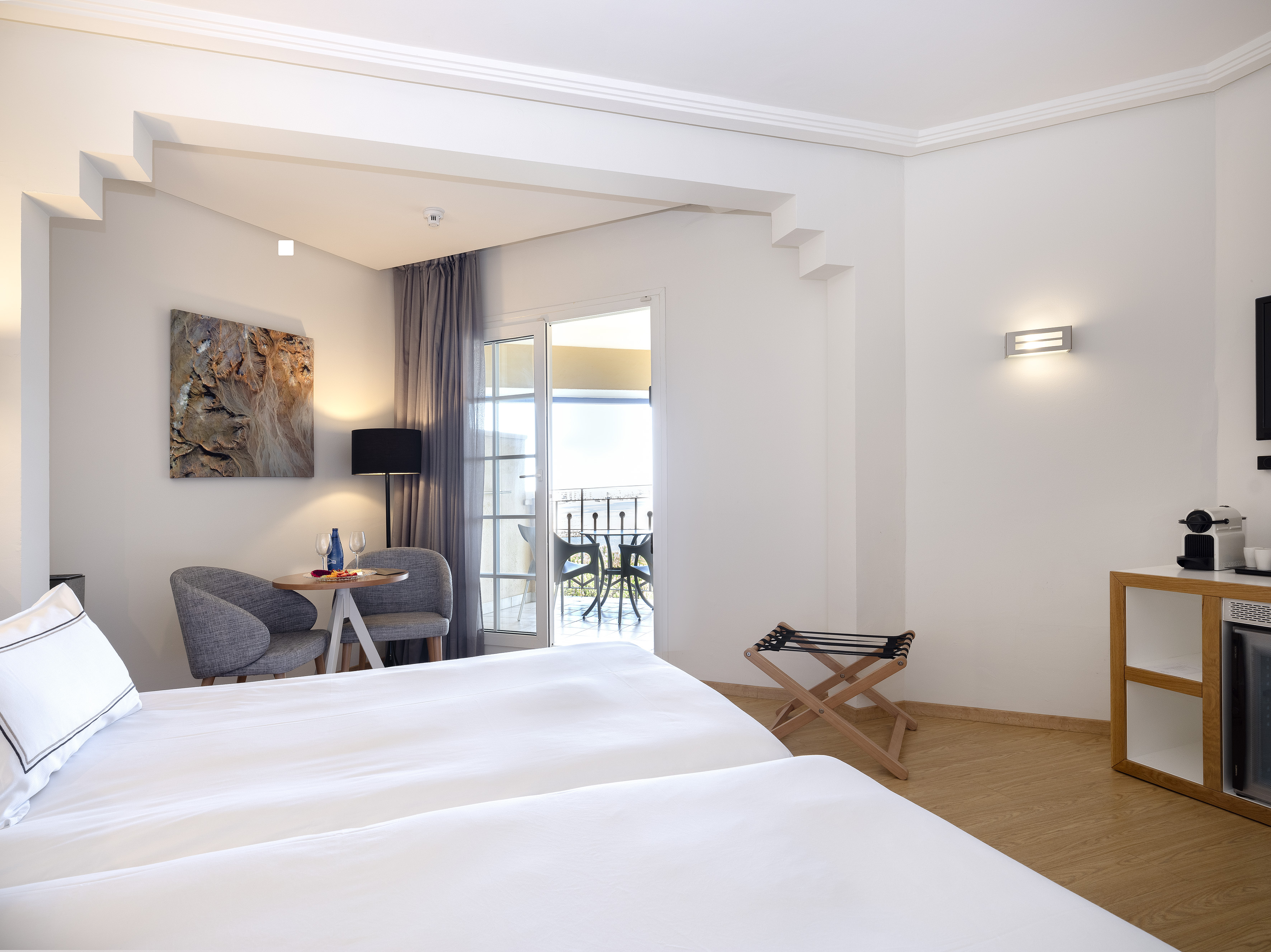 Modern hotel room with twin beds, balcony, and seating area.