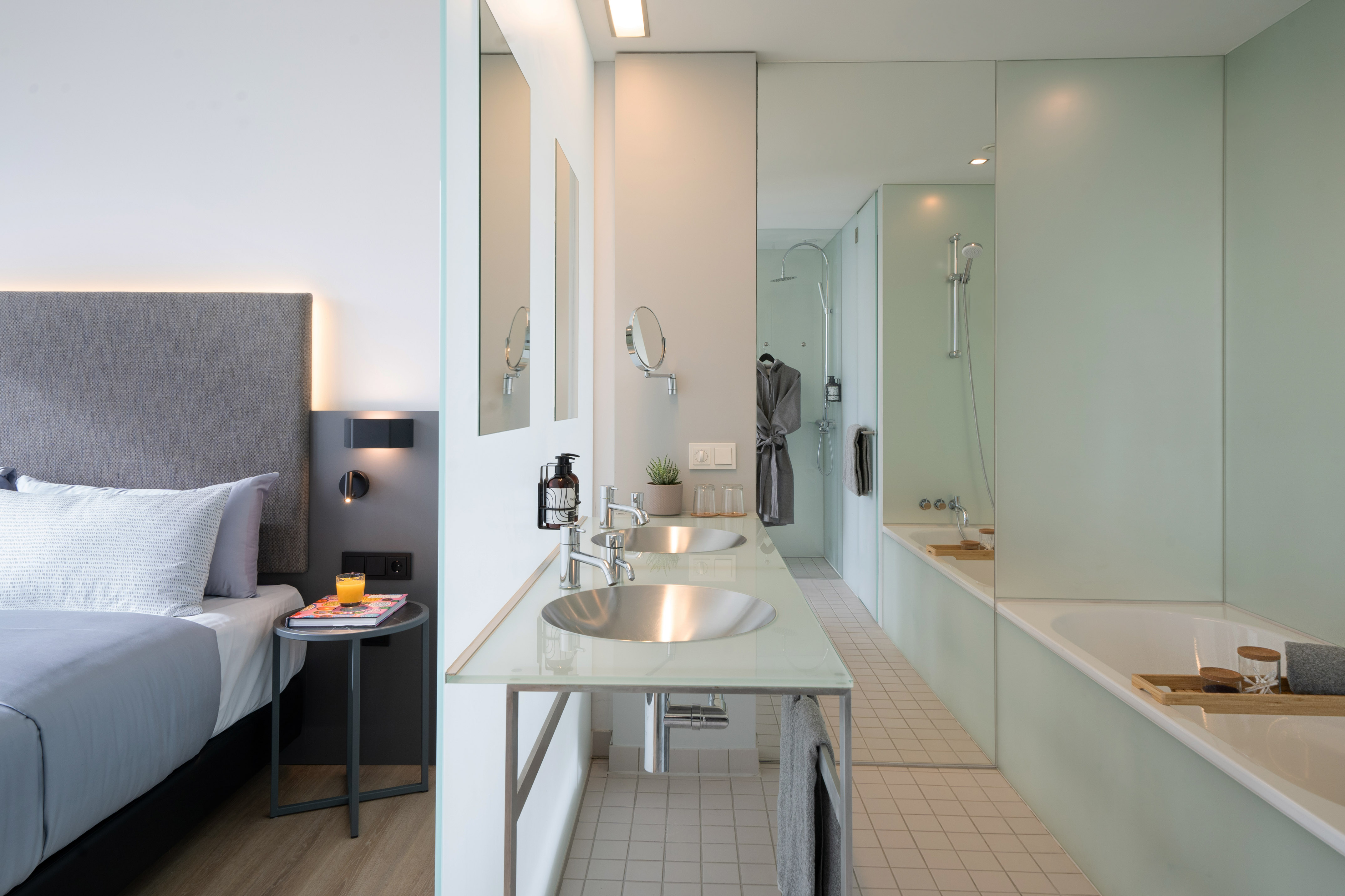 Modern hotel bedroom and open bathroom with double sinks, shower, and tub.