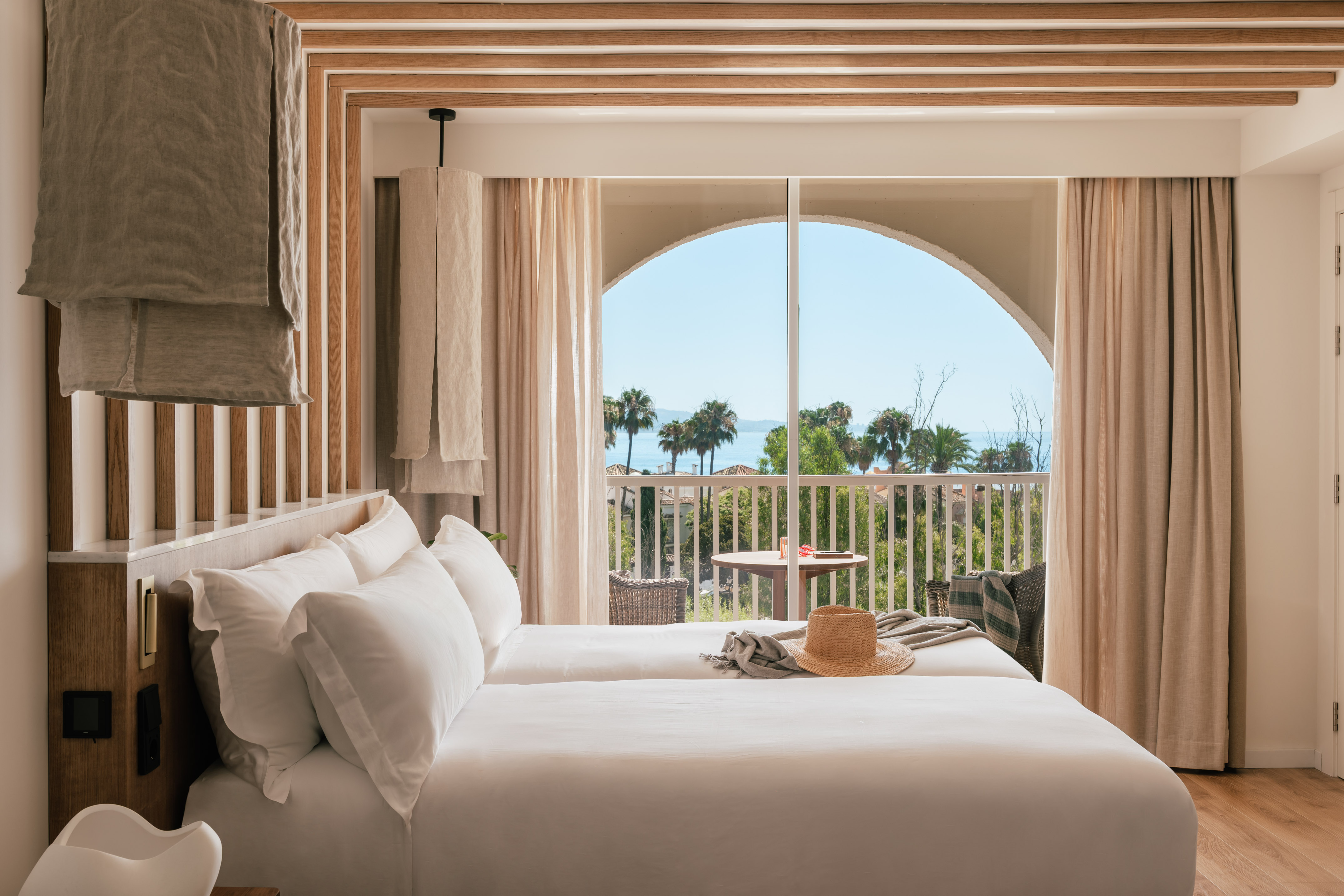 Modern hotel room with twin beds, sea view balcony, and palm trees.