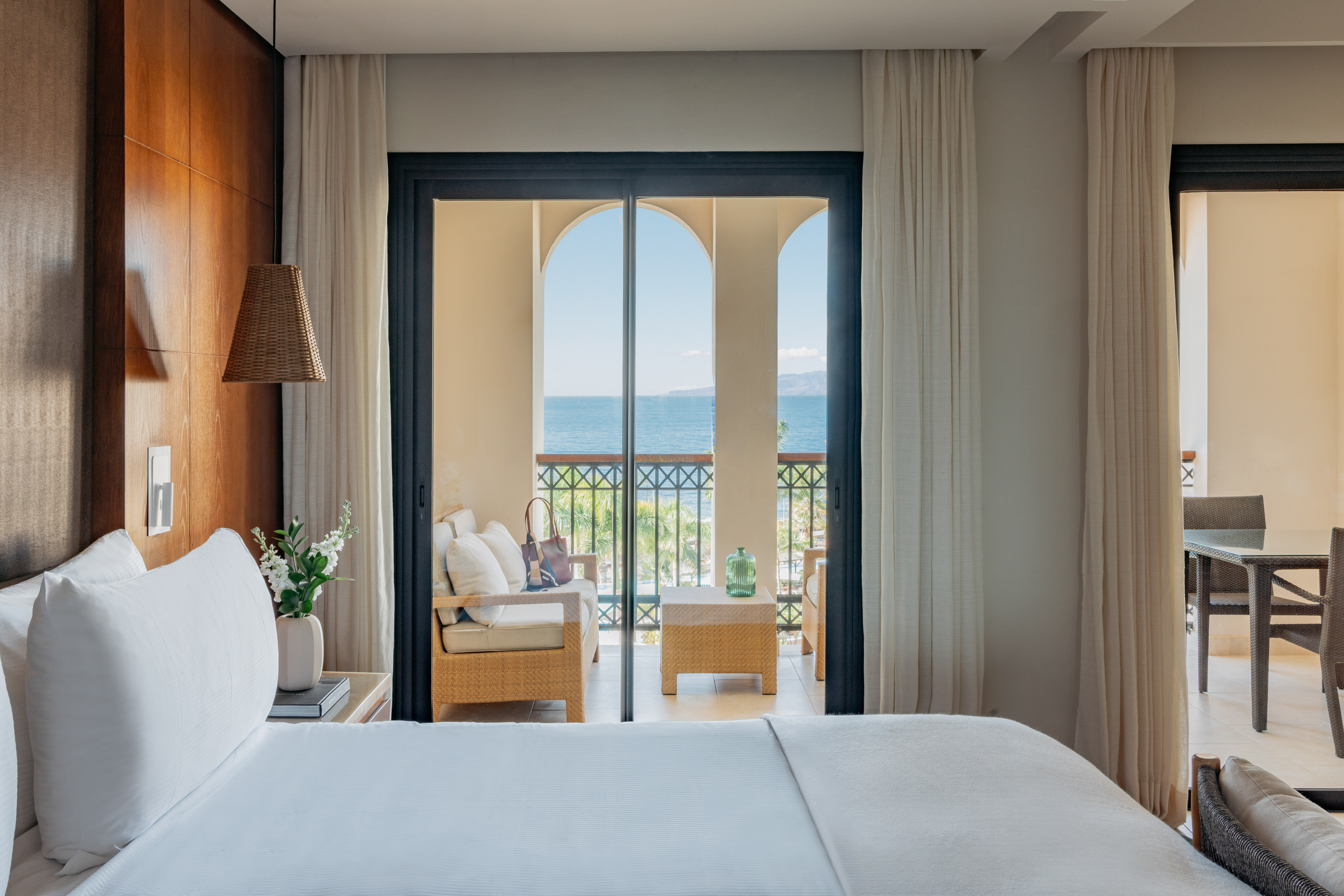Hotel room with white bed, balcony, and ocean view through arches.