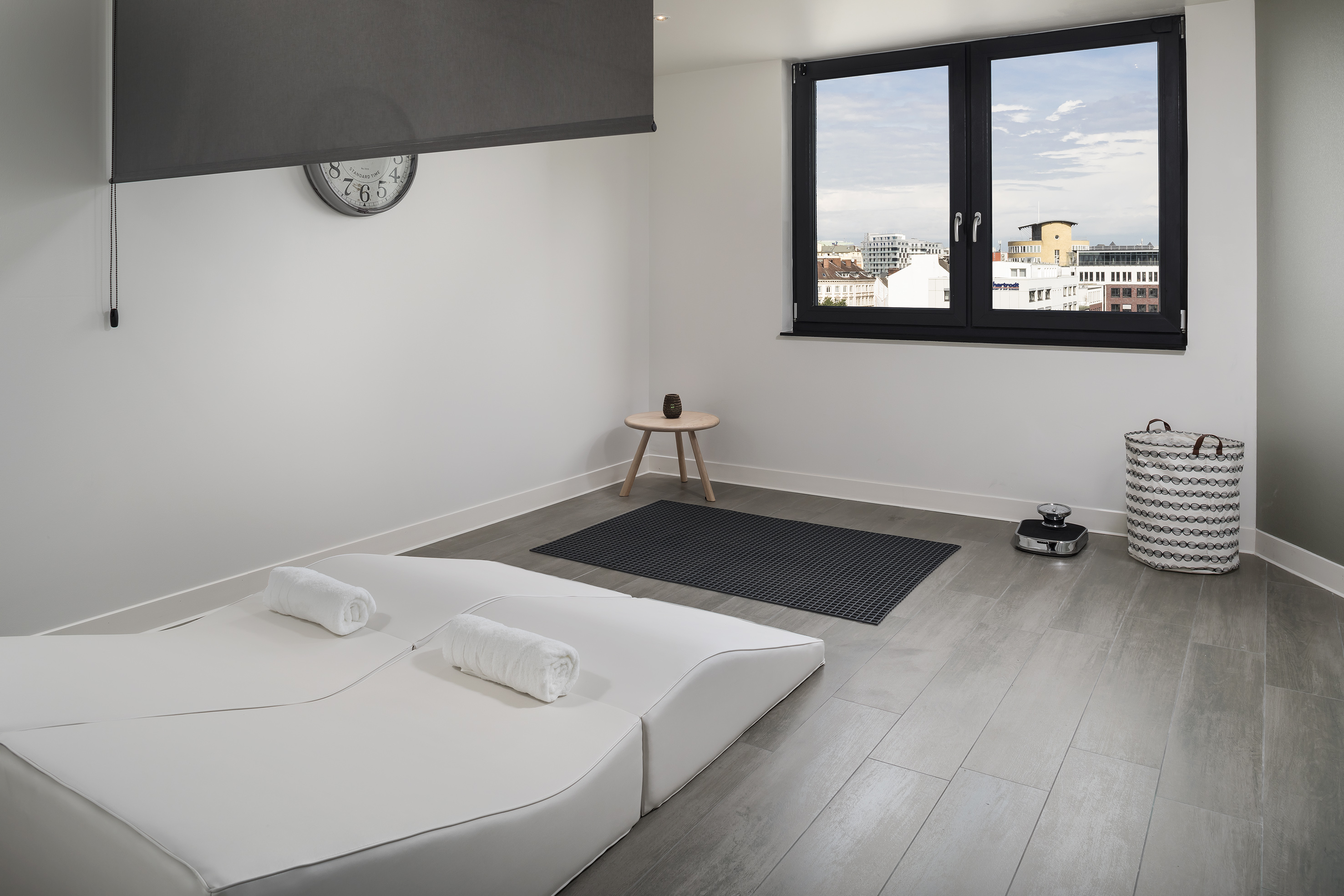 Minimalist wellness room with city view, white lounge bed, and yoga mat.