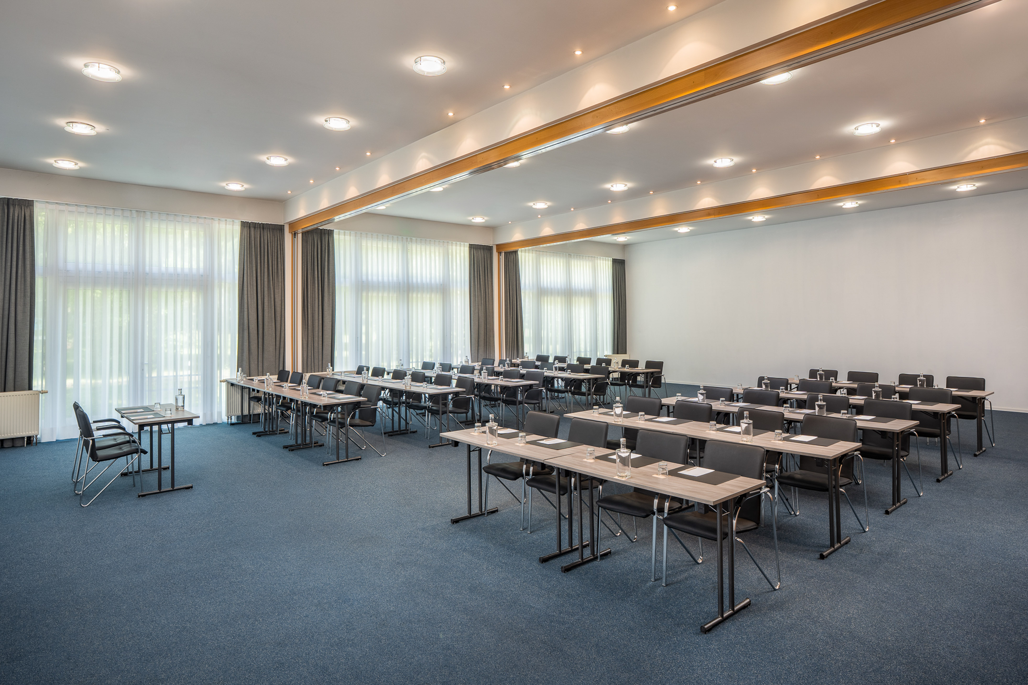 Spacious conference room with tables, chairs, blue carpet, and bright windows.
