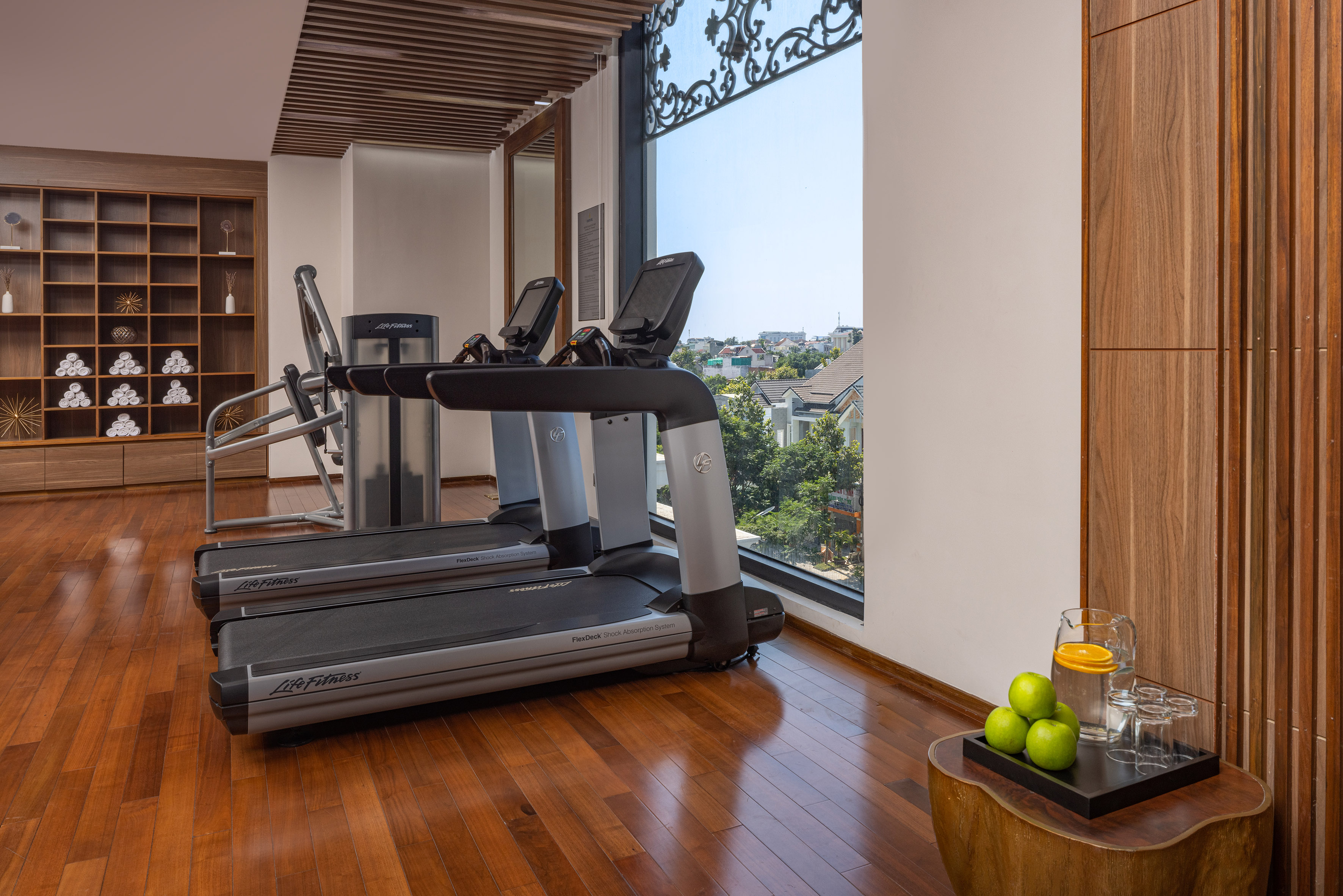 Modern gym with Life Fitness treadmills, city view, and hardwood floor.