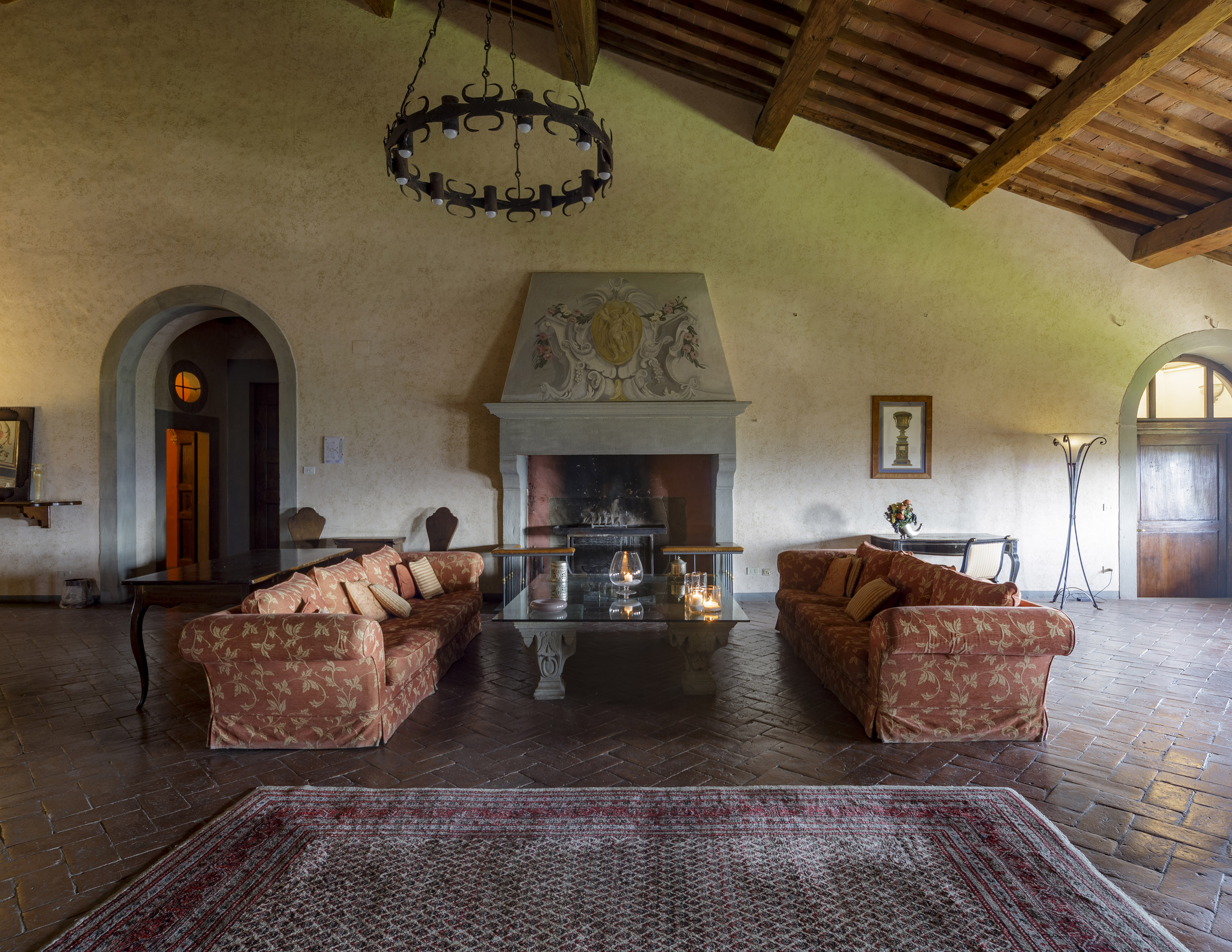 Rustic living room with exposed beams, fireplace, sofas, and terracotta floor.