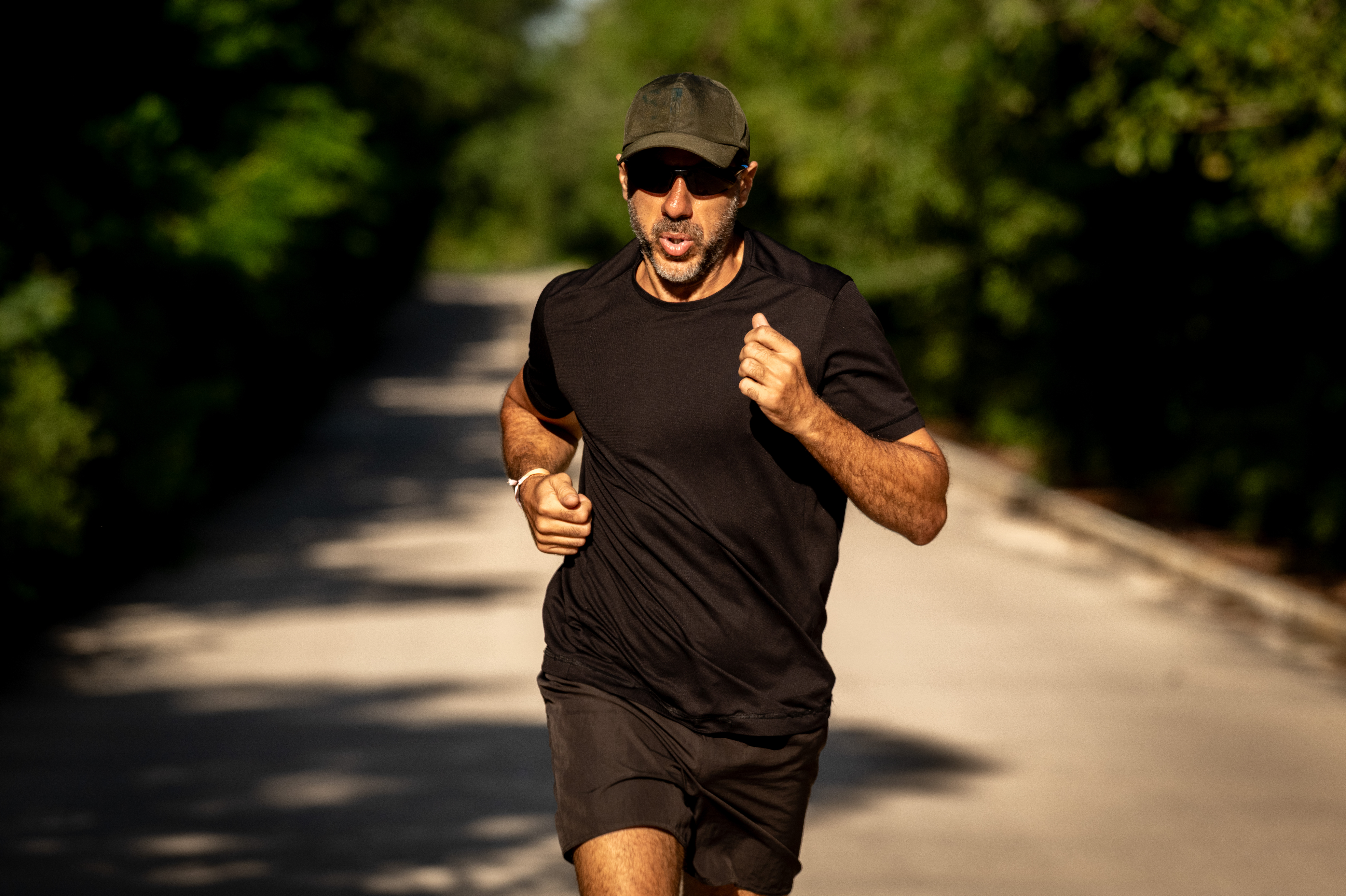 Fit man jogging outdoors in black activewear, sunglasses, and cap.
