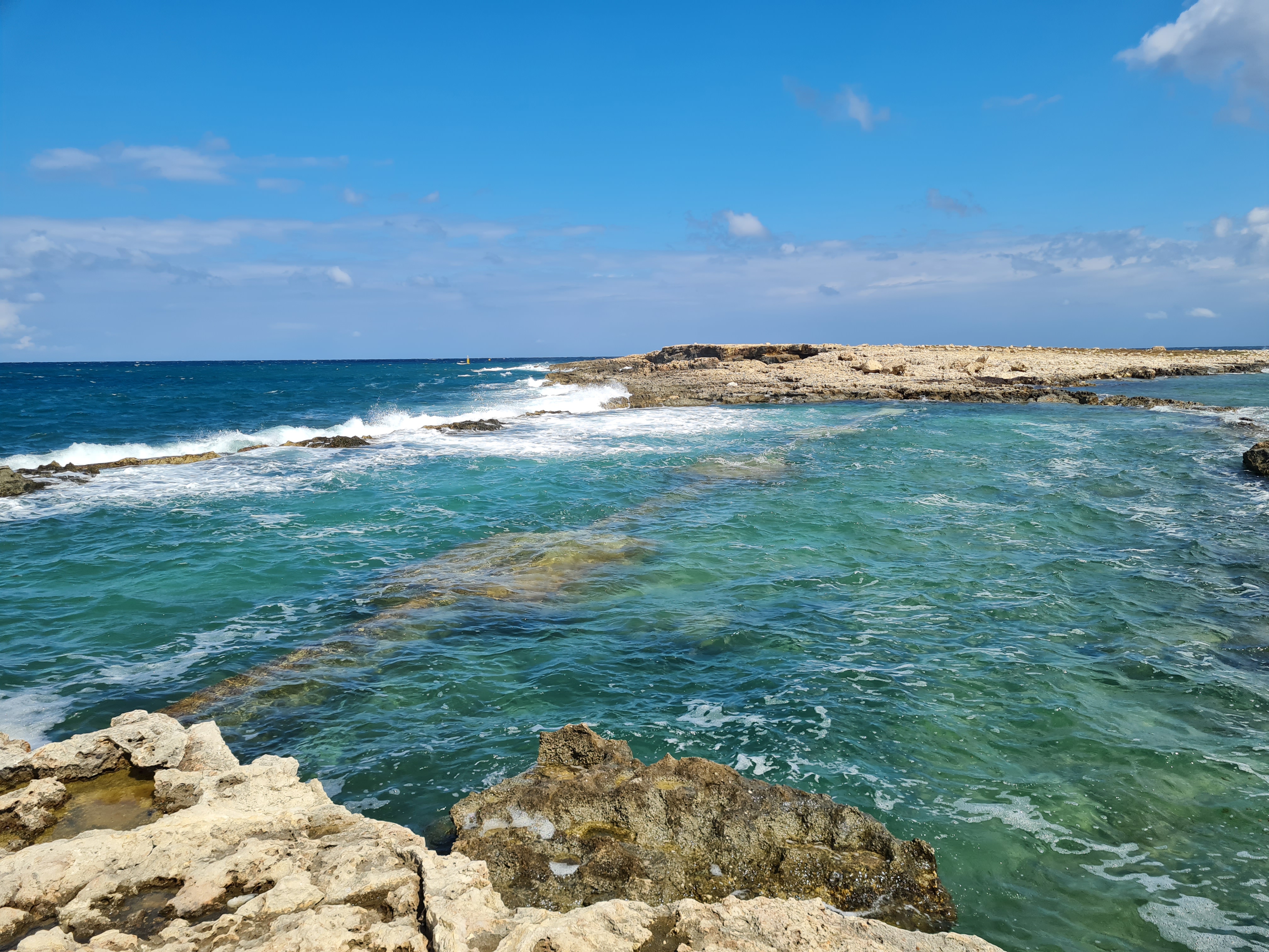 Rocky turquoise coastline with crashing waves under a bright blue sky.