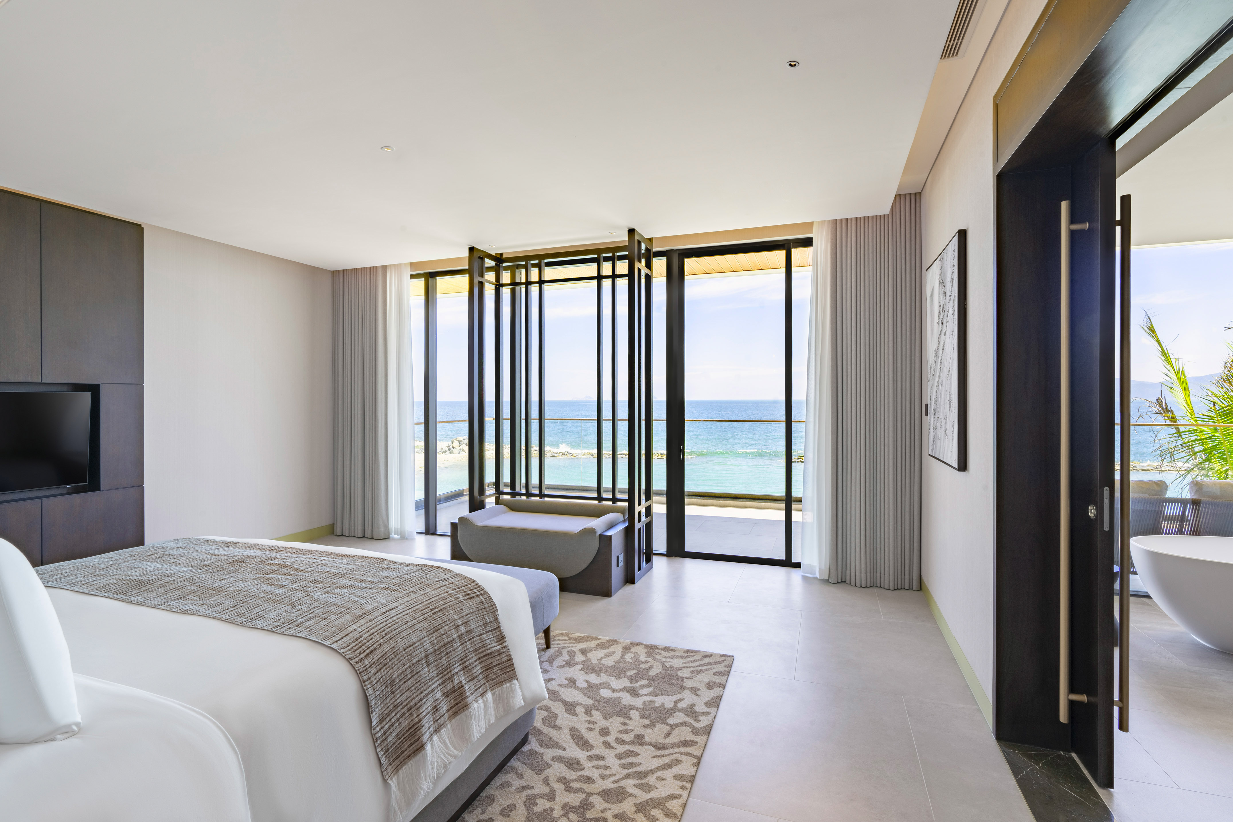 Luxury hotel bedroom with ocean view, large windows, and modern design.