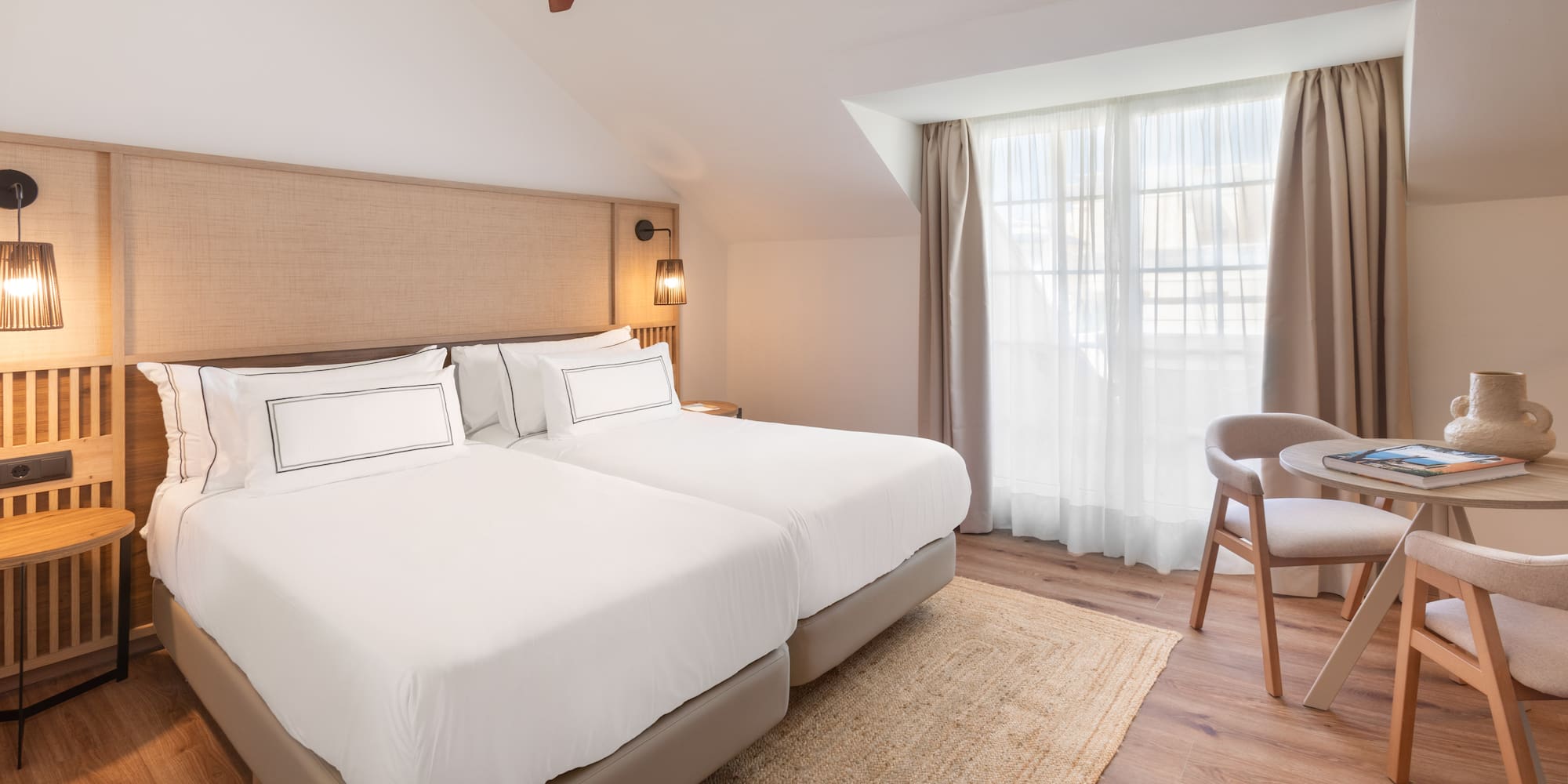 Attic room with twin beds, wooden ceiling fan, window, and small table.