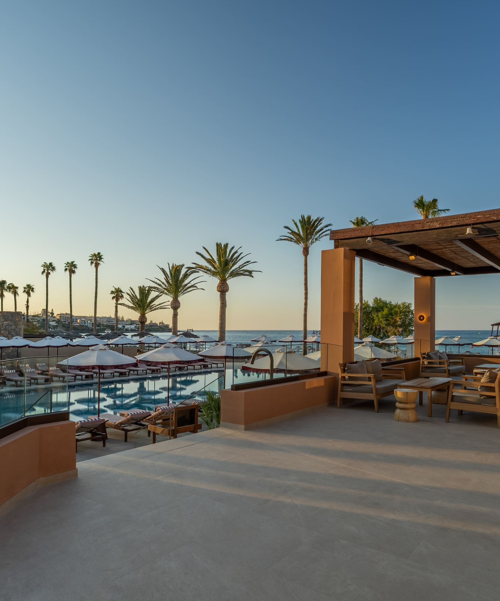 Luxury resort pool, patio, and beach with ocean view, palm trees, and seating.