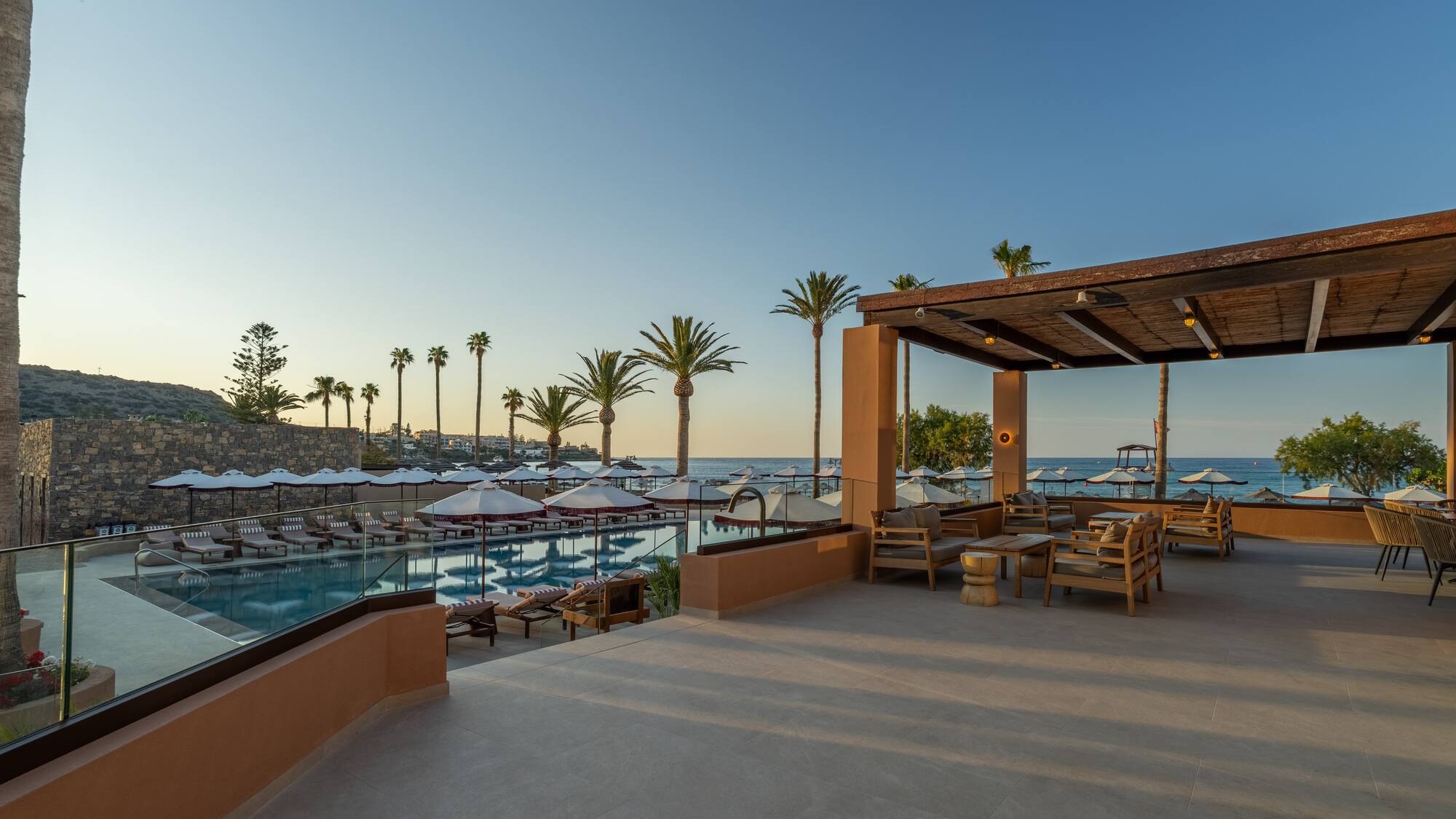 Tropical resort pool and patio with ocean view, palm trees, and lounge seating.