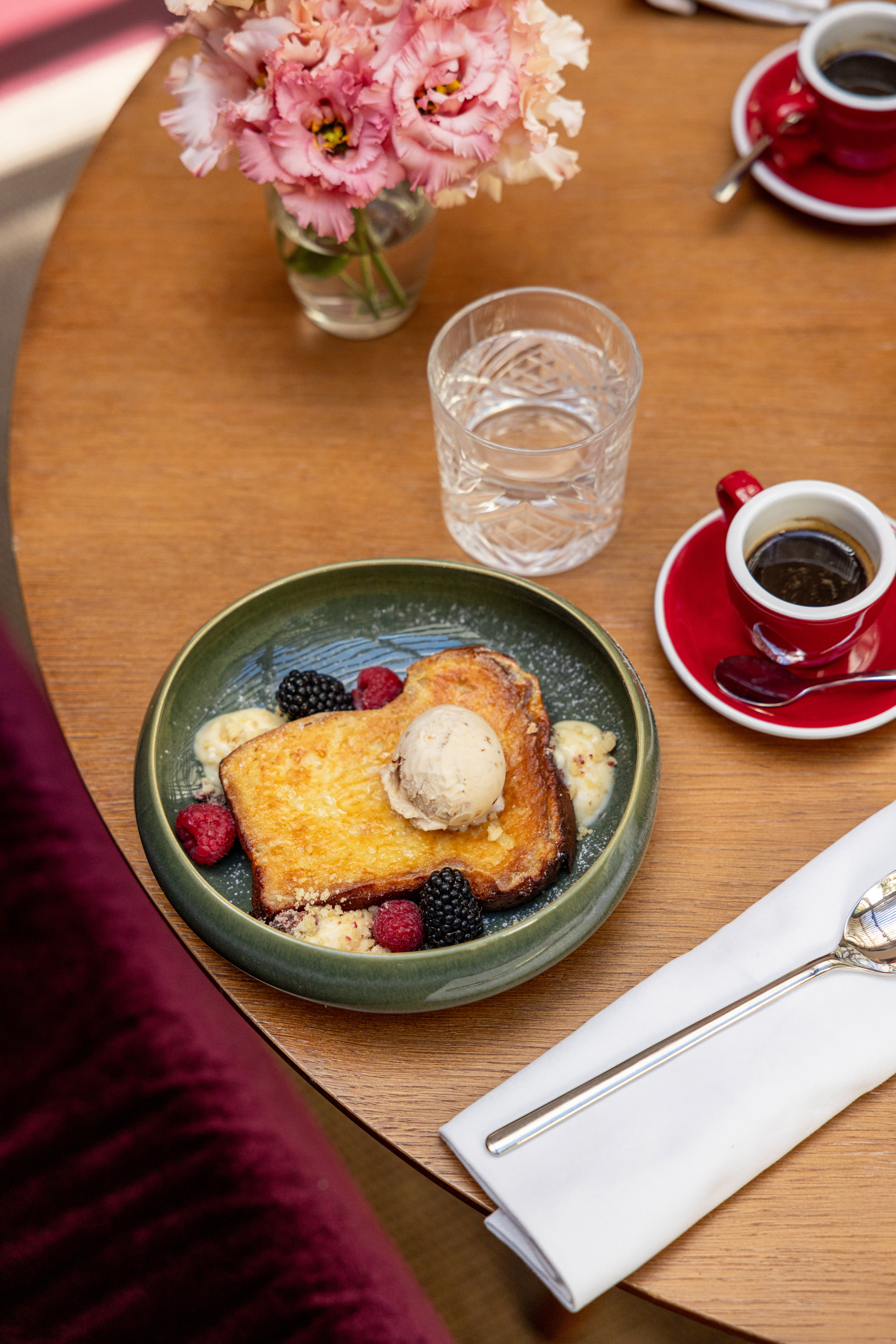 French toast with ice cream, fresh berries, espresso, and flowers on wooden table.