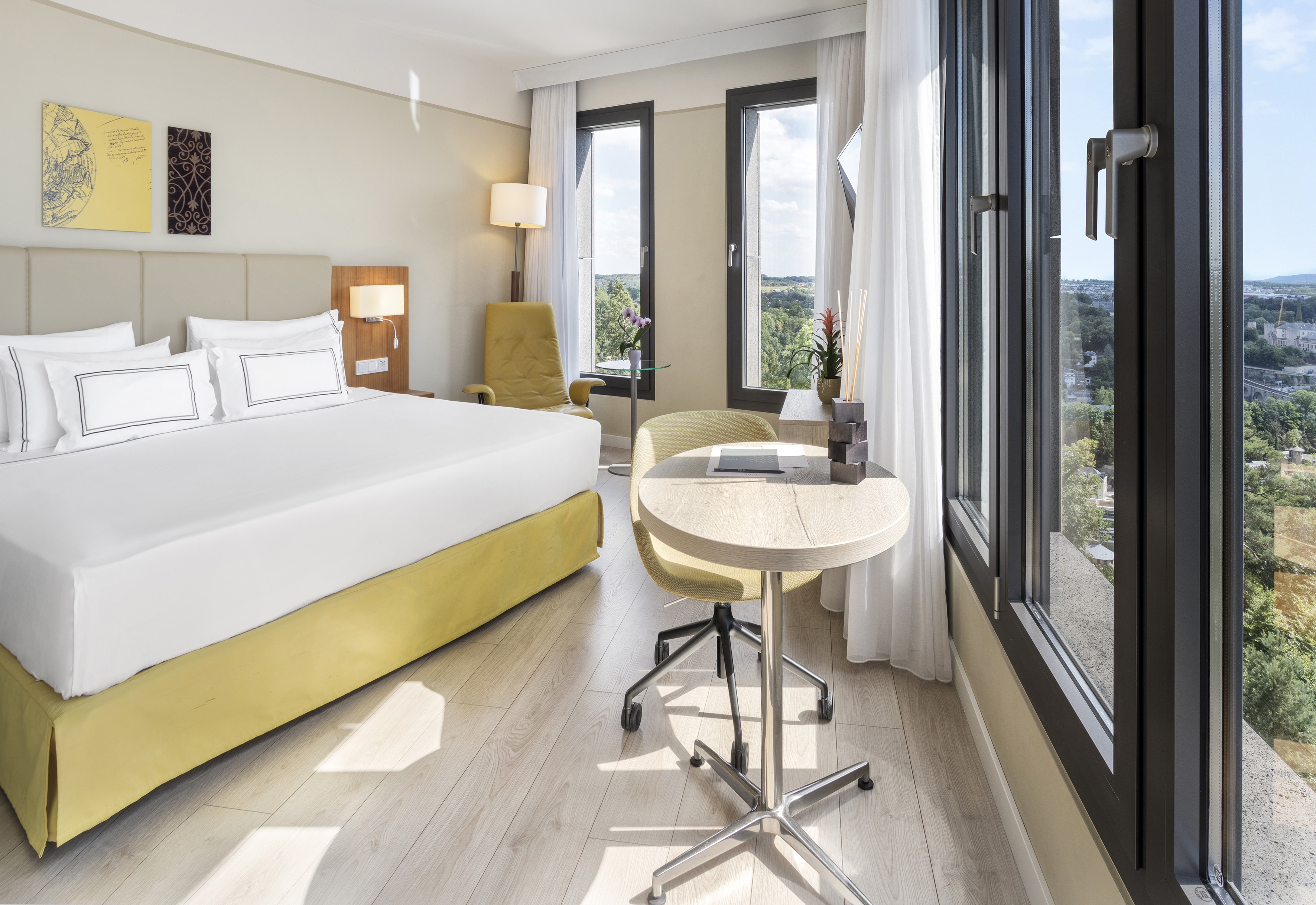 Bright modern hotel bedroom with yellow bed, scenic window view, and desk.