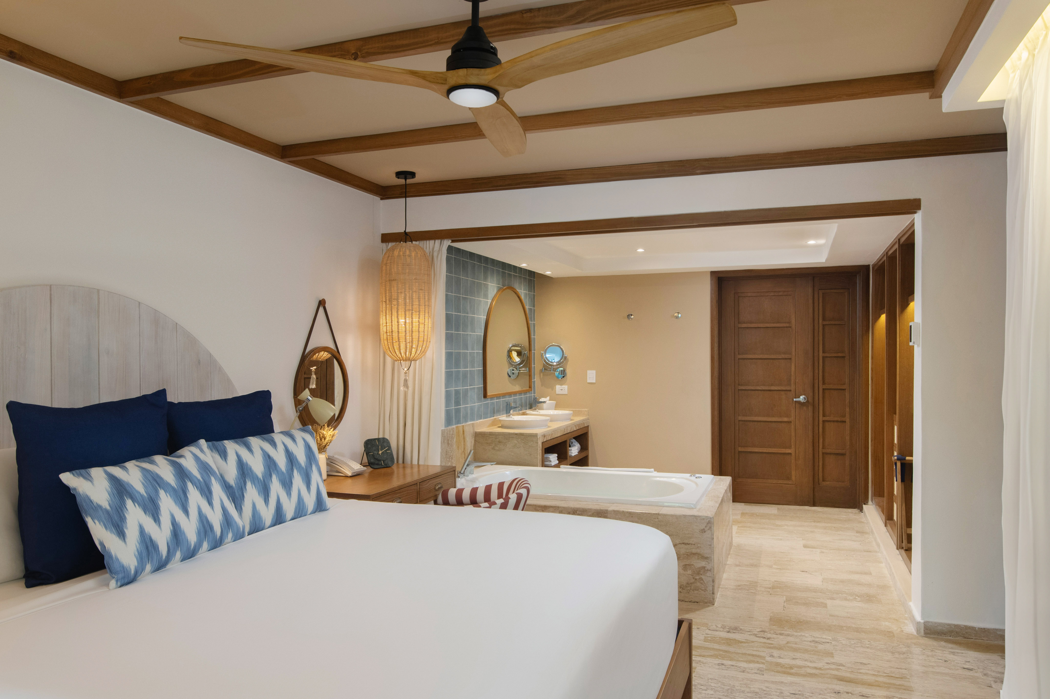 Modern hotel bedroom with open concept bathroom, tub, and tropical decor.