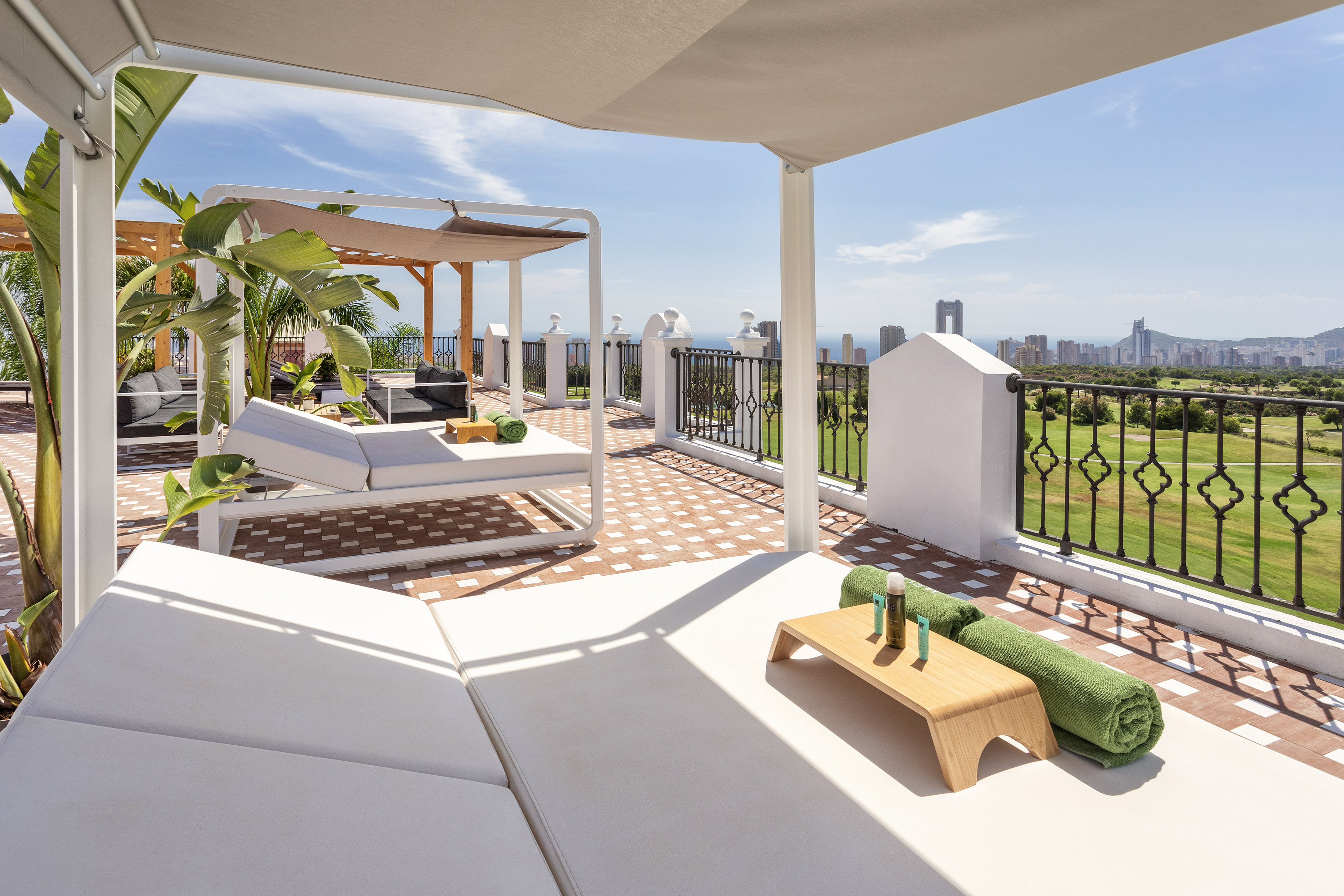 Luxury rooftop terrace with sun loungers, golf course, and city skyline.