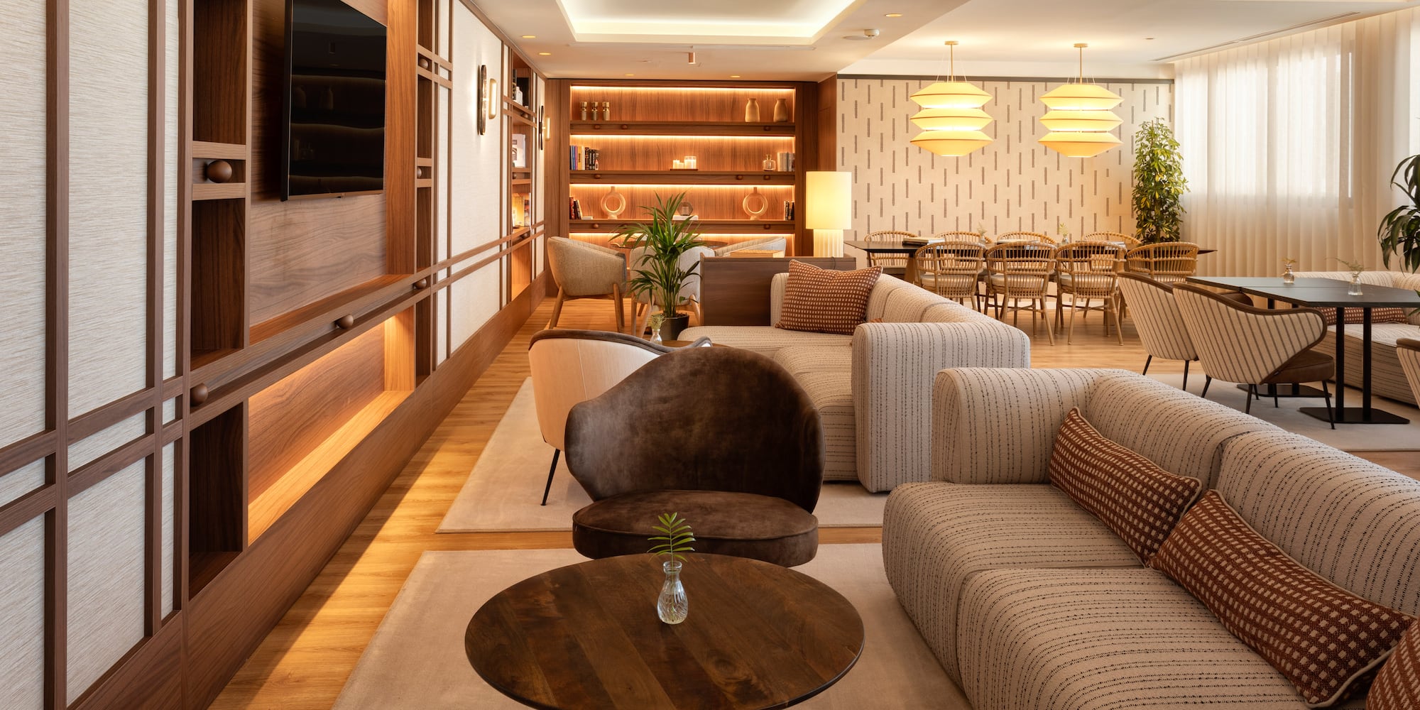 Lobby moderno con sofás cómodos, pared de madera retroiluminada y zona de comedor.