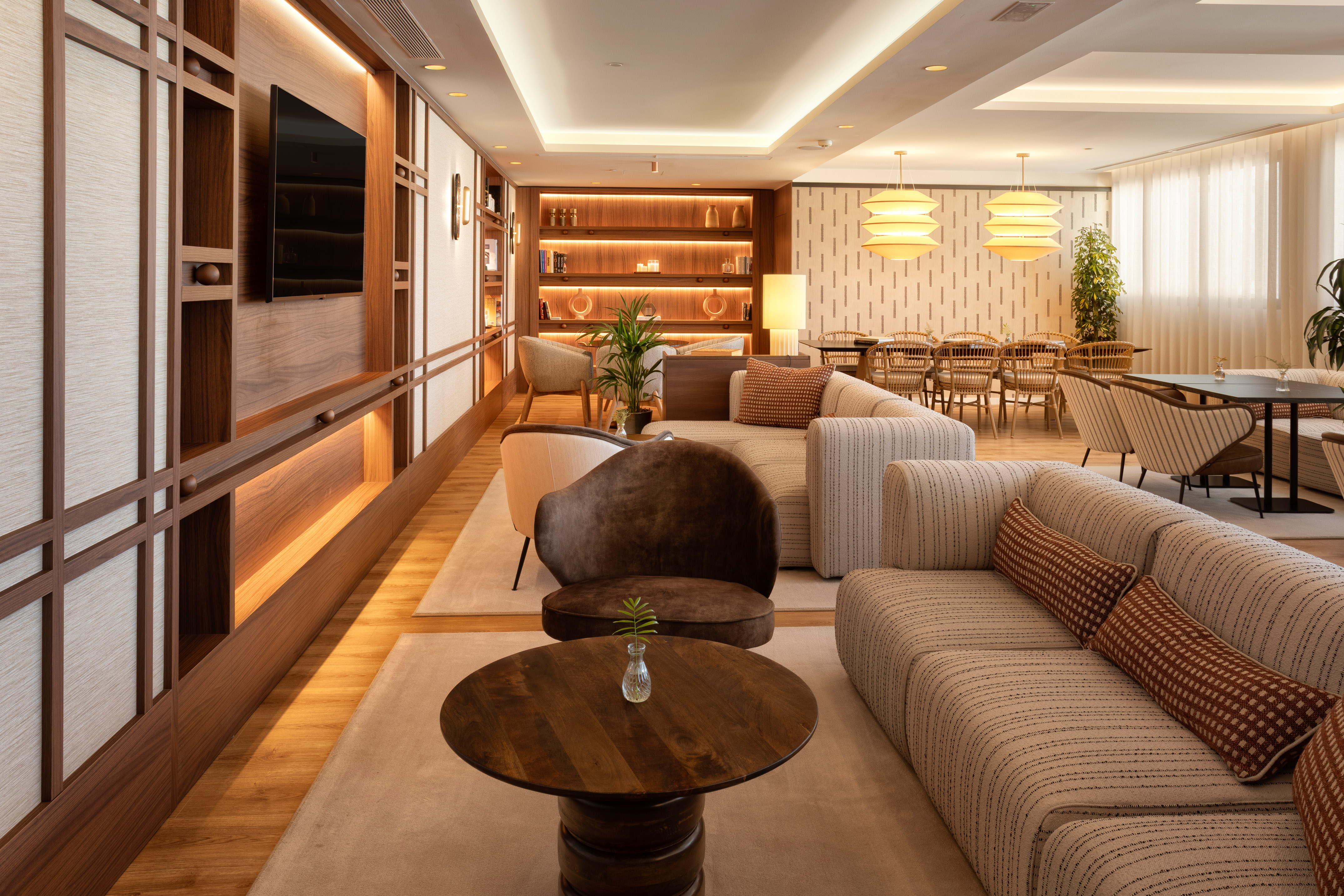 Lobby moderno con sofás cómodos, pared de madera retroiluminada y zona de comedor.