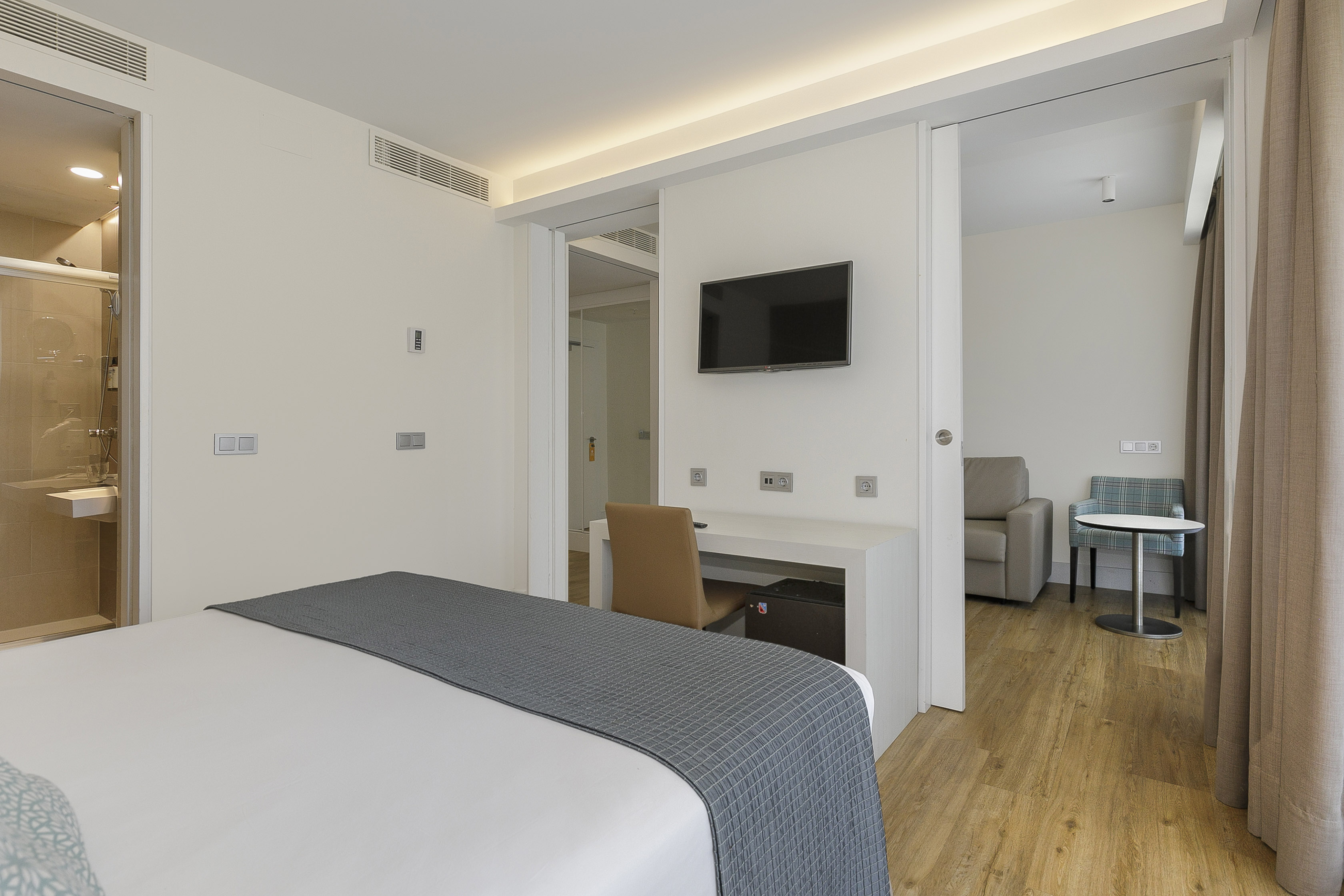 Modern hotel suite with bed, desk, TV, separate lounge, and bathroom.