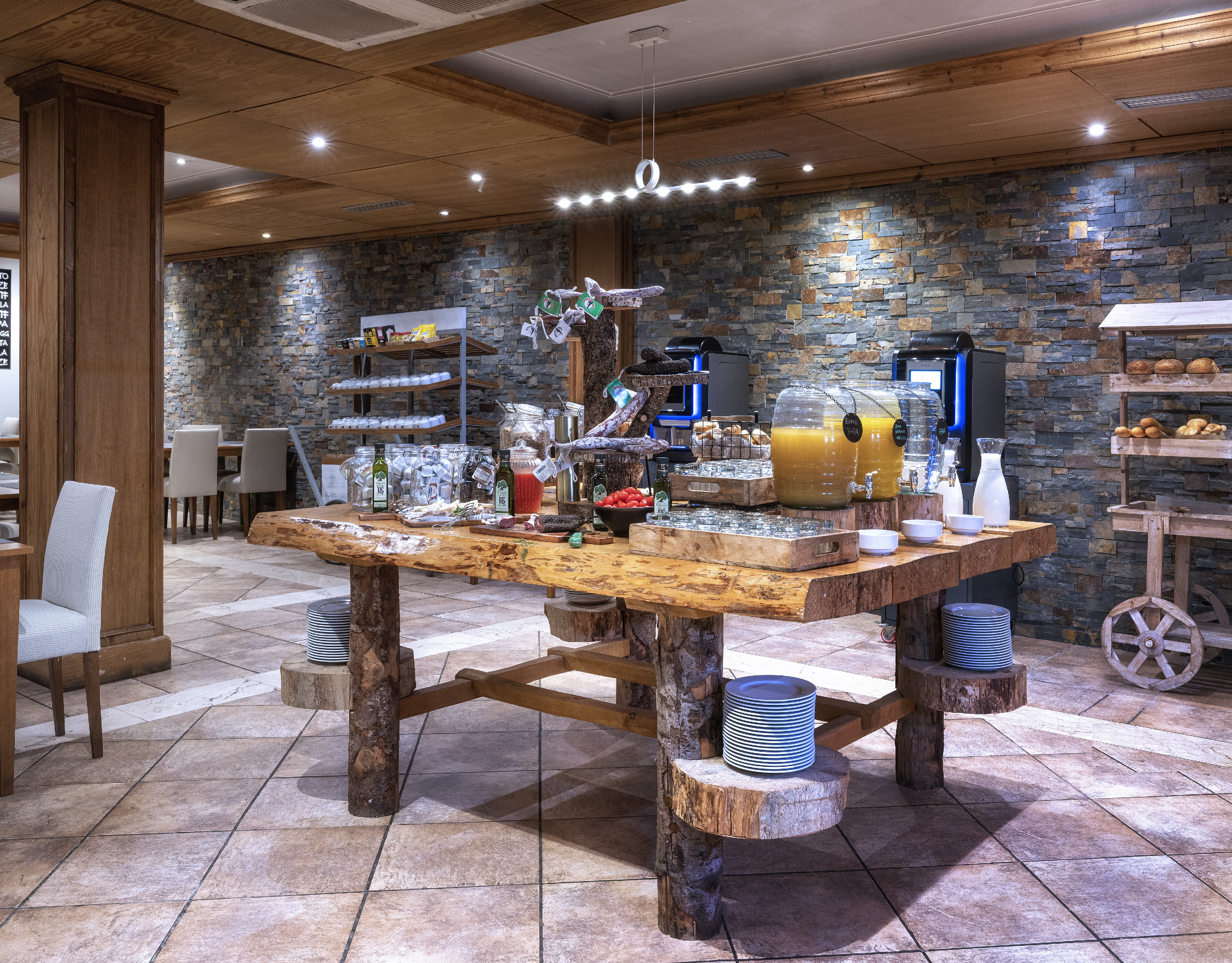 Cozy hotel breakfast buffet with rustic wood table, food, and juice dispensers.