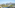Scenic balcony view of a sunny town, green trees, and distant mountains.