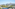 Scenic balcony view of a sunny town, green trees, and distant mountains.