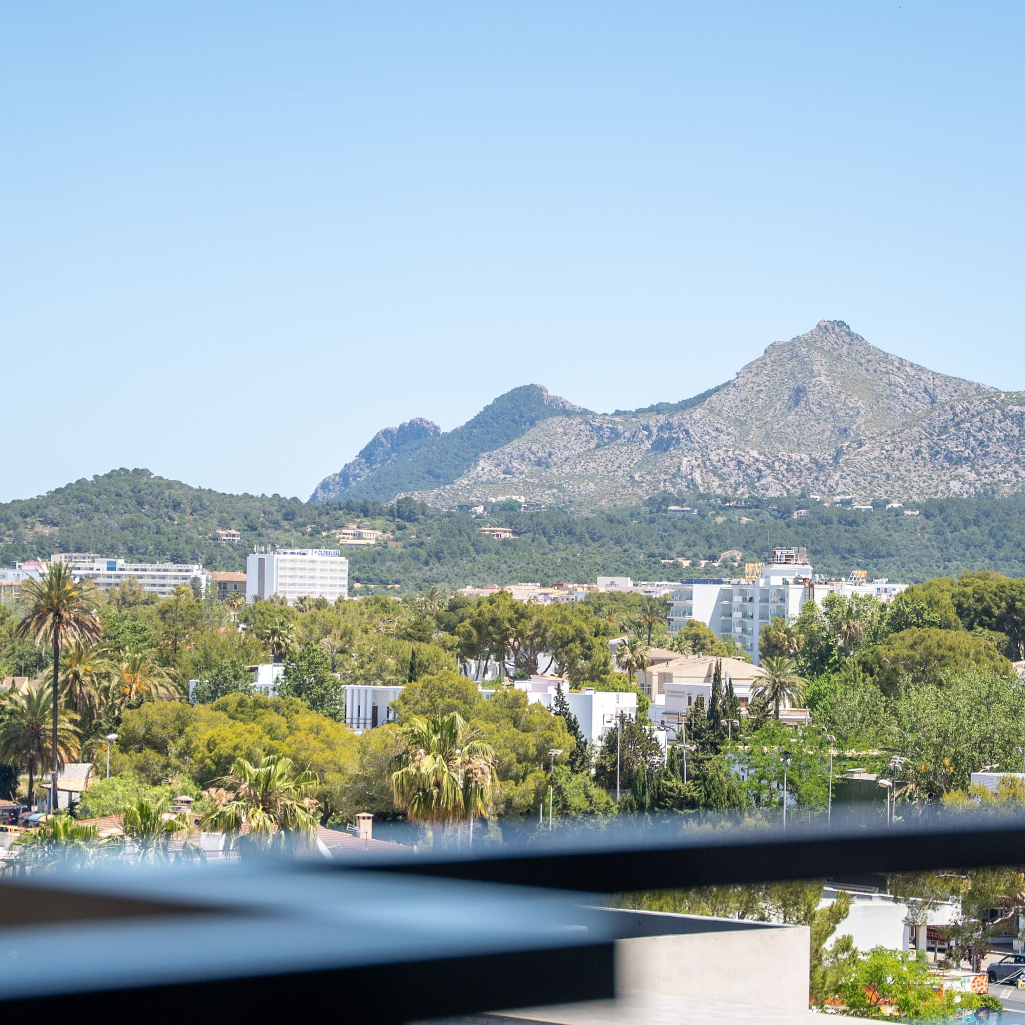 Scenic balcony view of a sunny town, green trees, and distant mountains.
