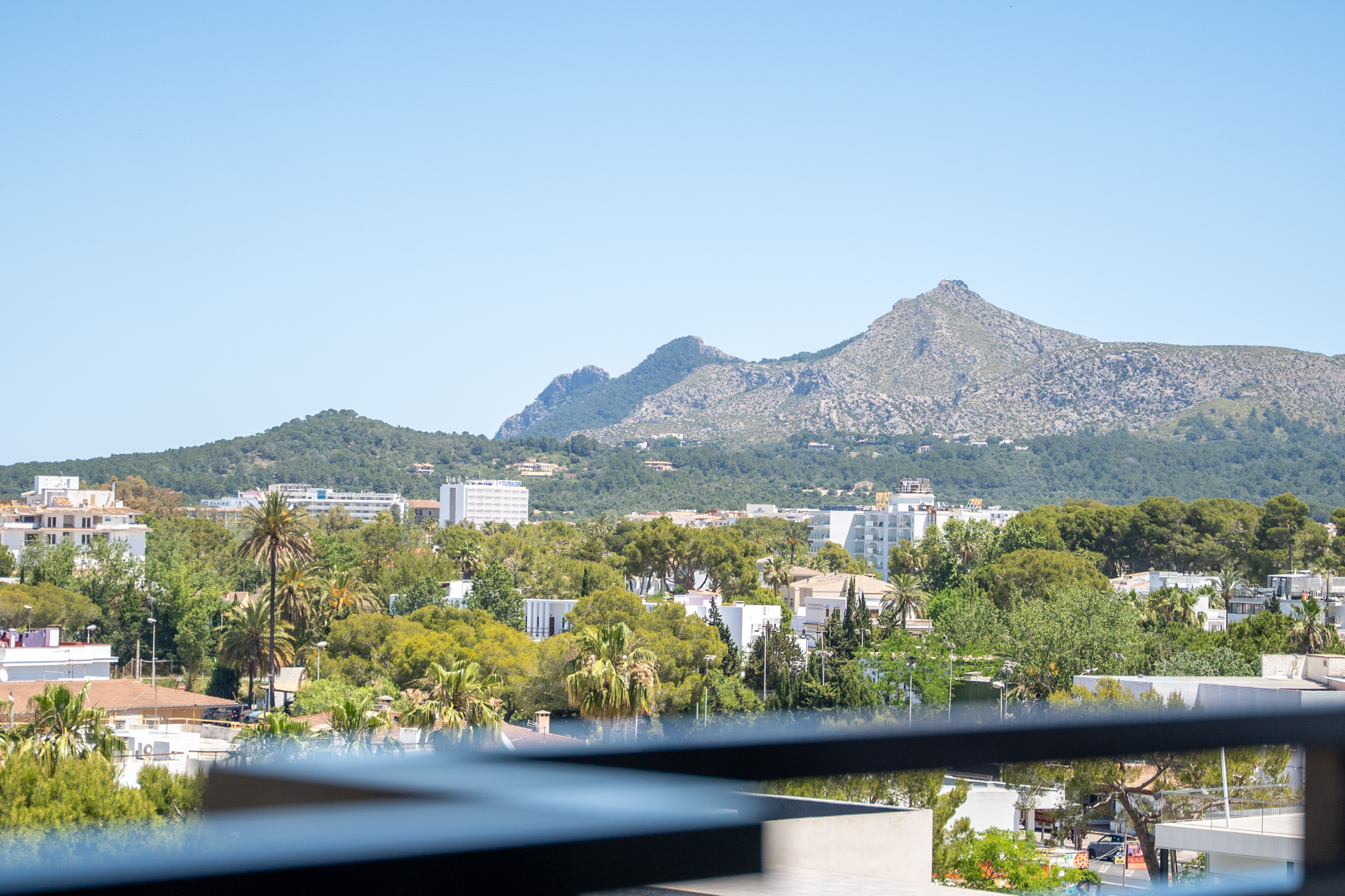 Scenic balcony view of a sunny town, green trees, and distant mountains.