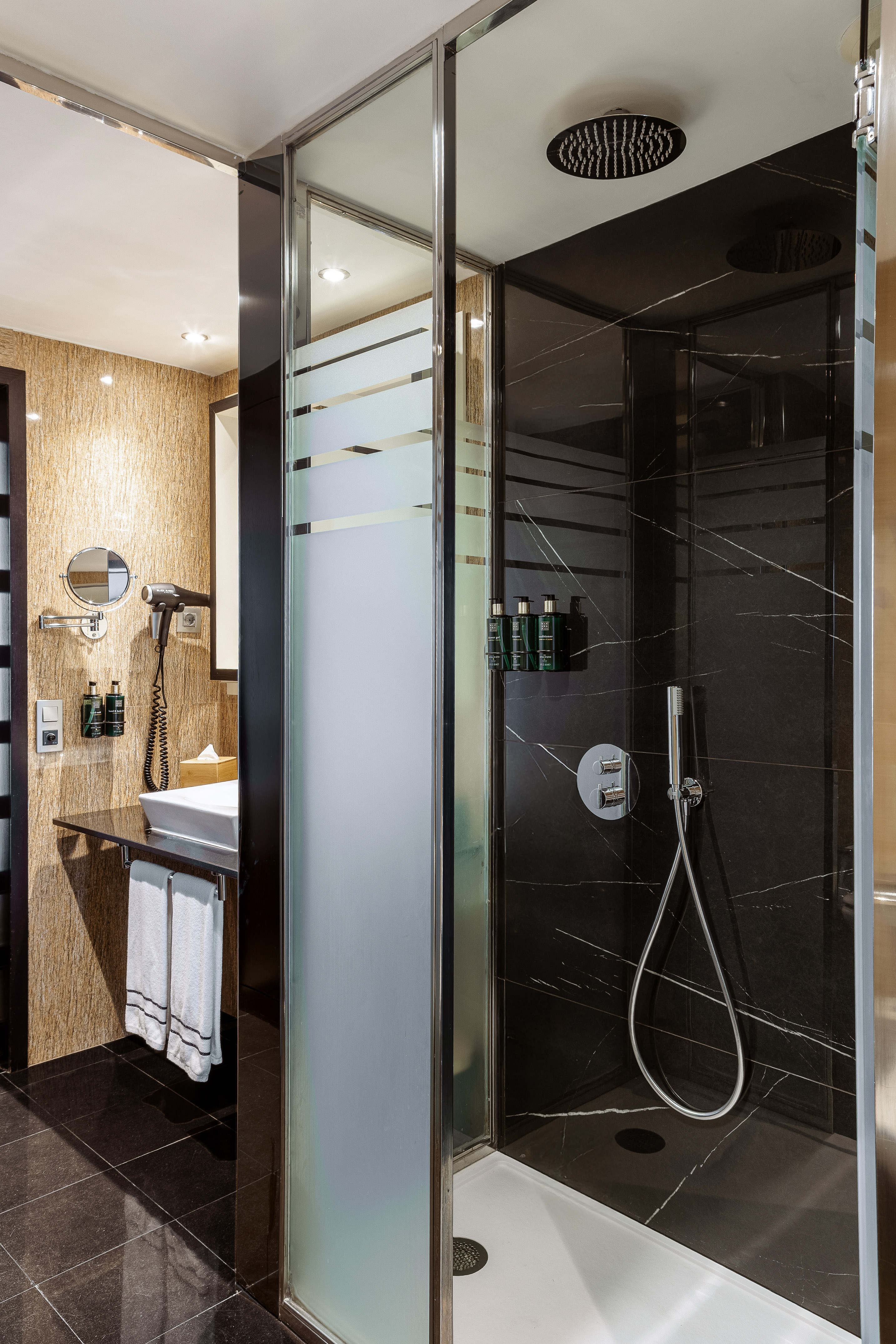 Modern bathroom with black marble shower, glass partition, and vanity area.