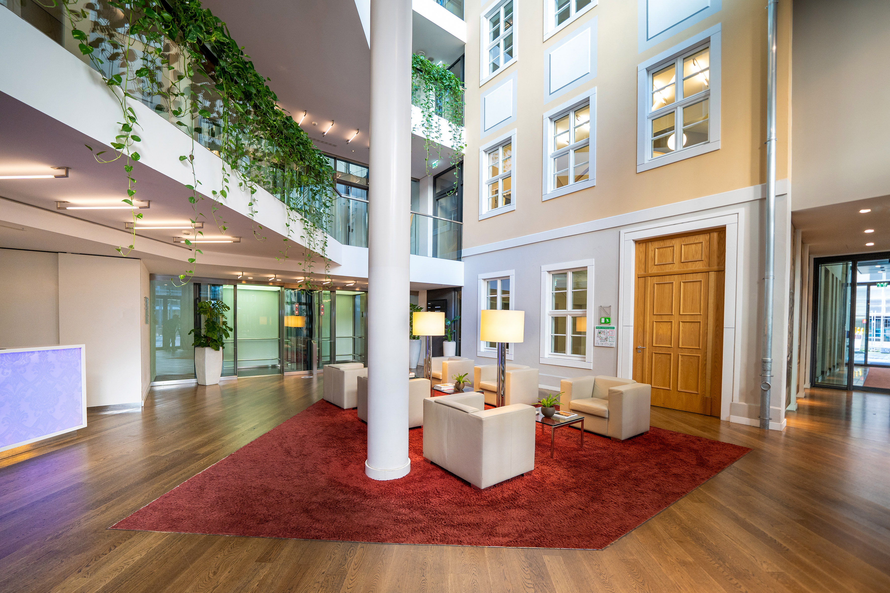 Contemporary lobby featuring a red rug lounge, pillar, and greenery.