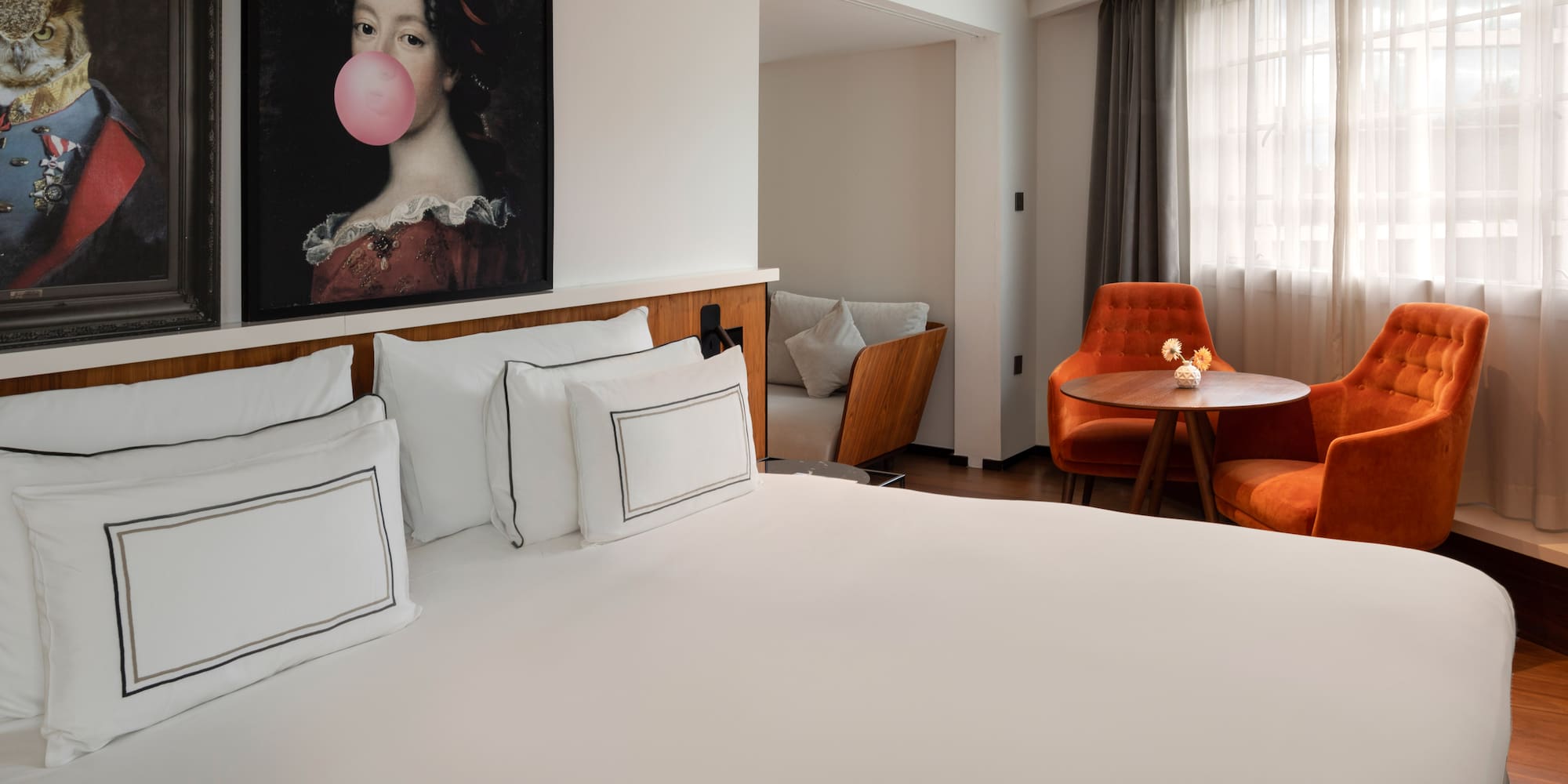 Boutique hotel bedroom with white bed, pop art, and orange velvet chairs.