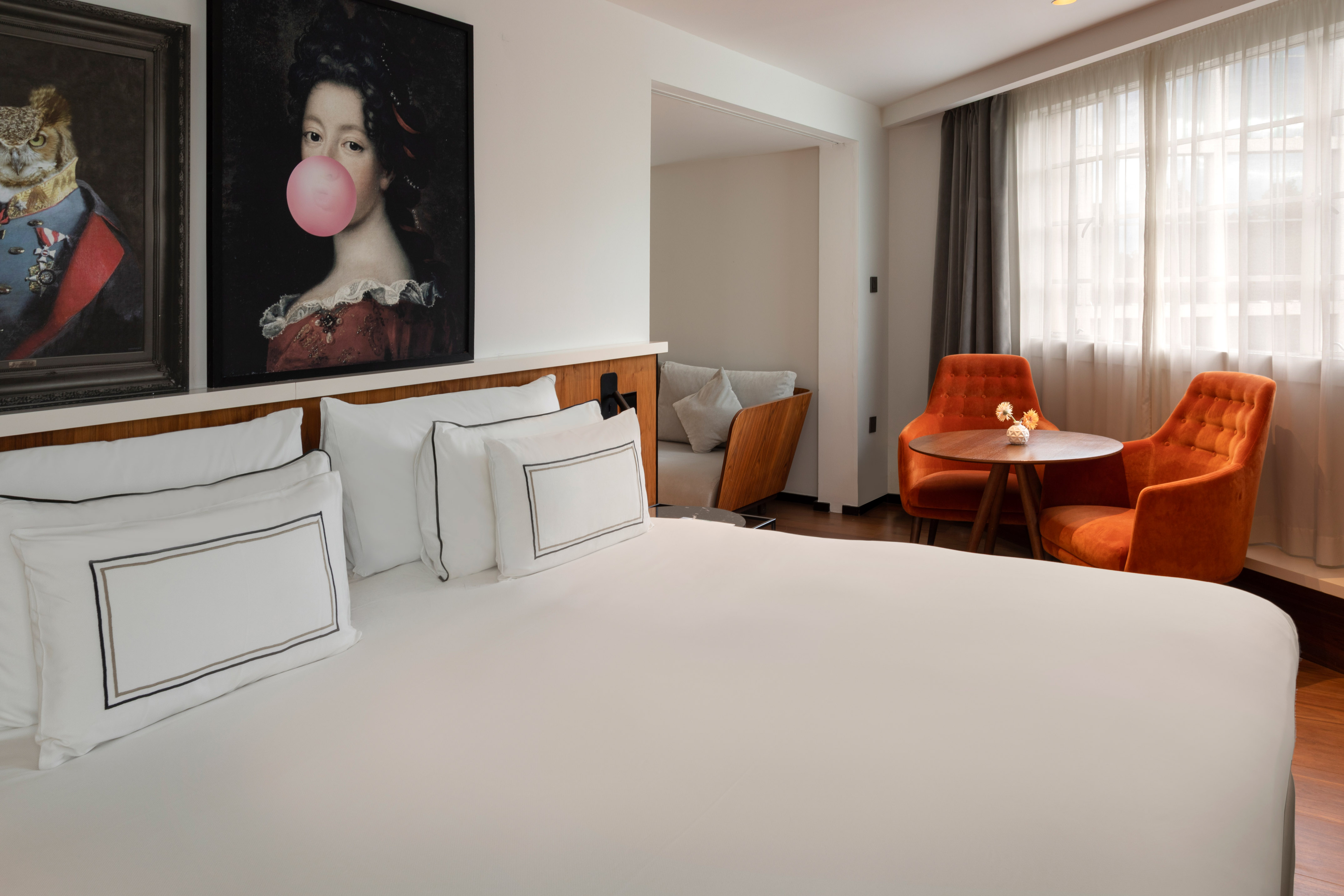 Boutique hotel bedroom with white bed, pop art, and orange velvet chairs.