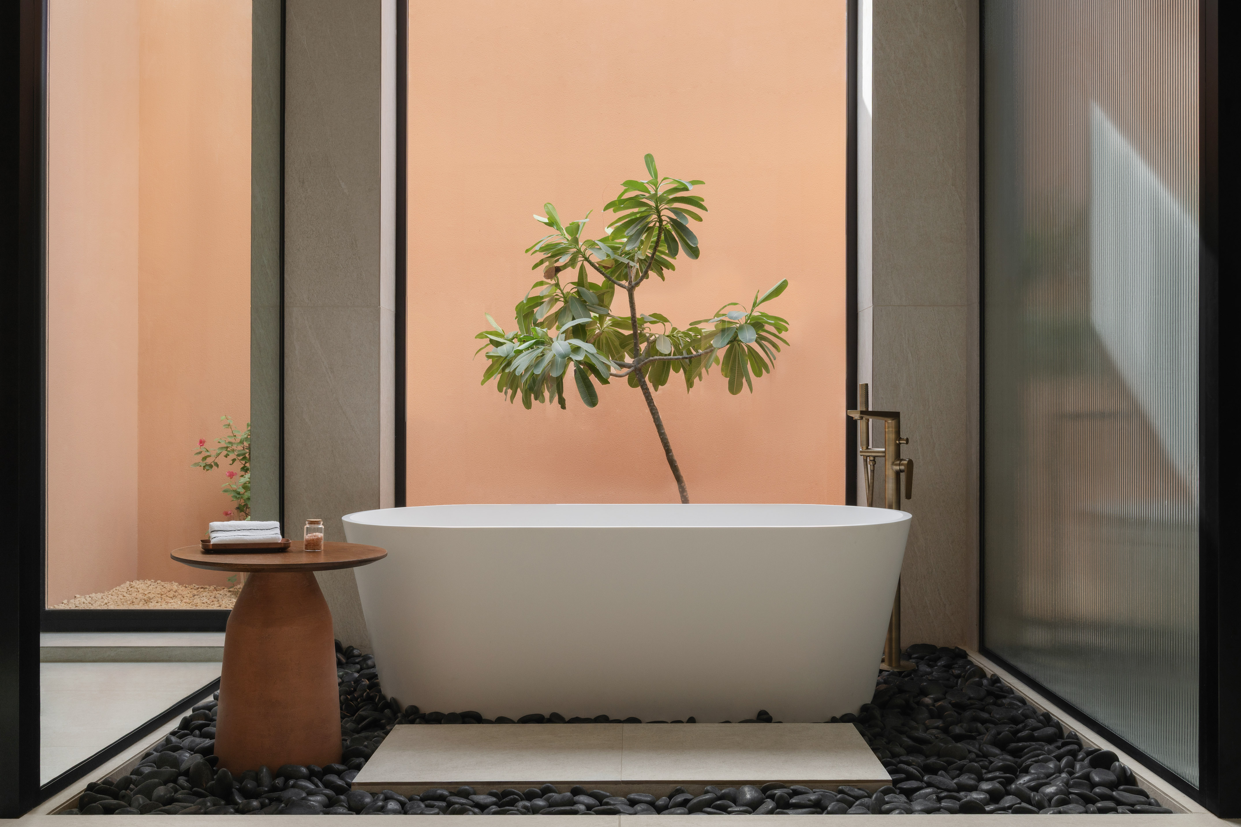 Modern freestanding tub in spa bathroom with tropical plant and river rocks.