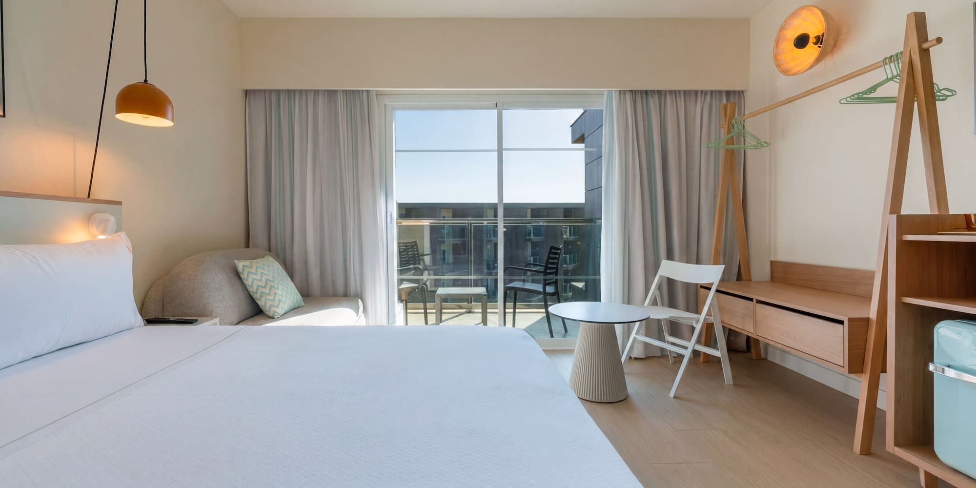 Bright minimalist hotel room with white bed, balcony, and wooden furnishings.