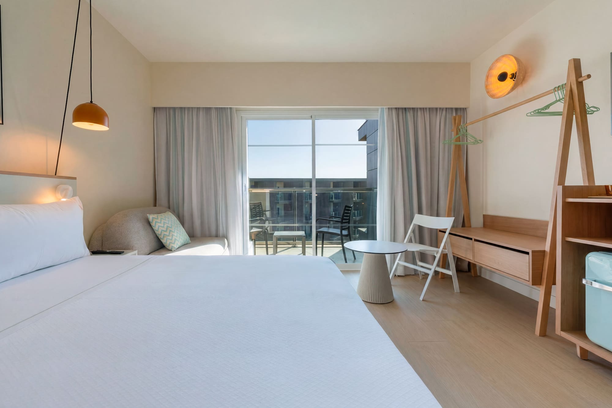 Modern hotel room with large bed, balcony, and contemporary wooden furniture.