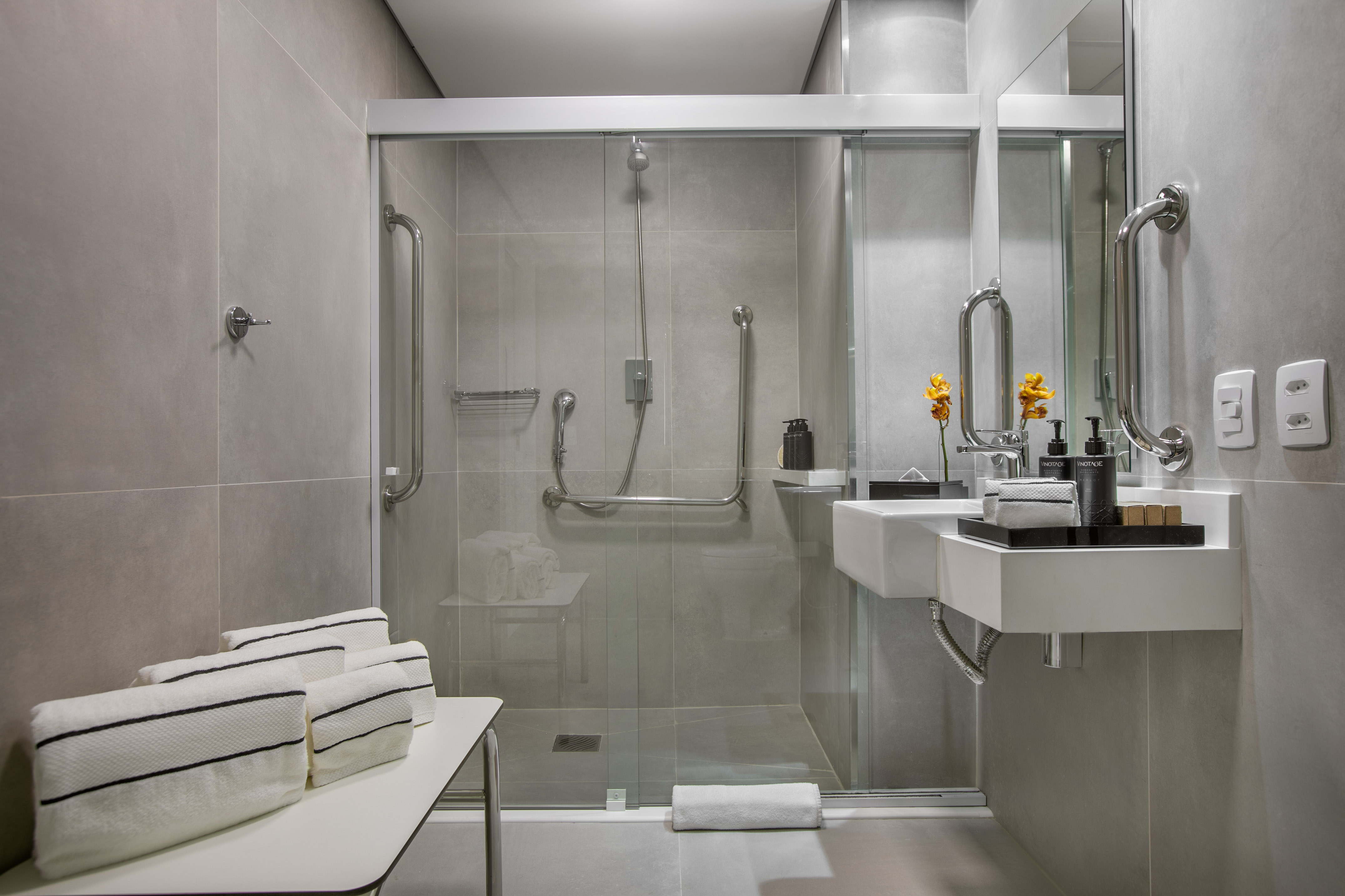 Modern accessible bathroom with walk-in shower, grab bars, and floating vanity.