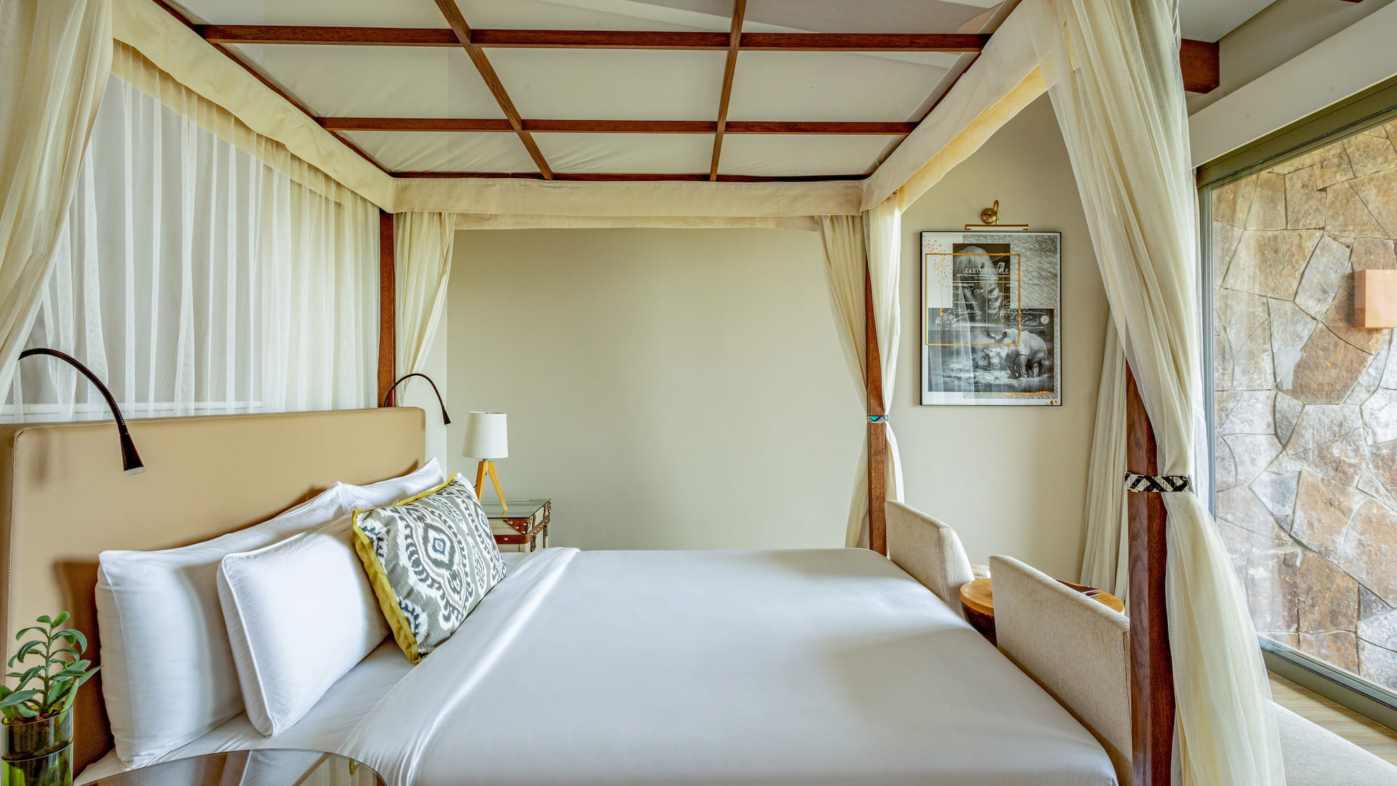 Luxury four-poster canopy bed with white linens in an elegant hotel room.