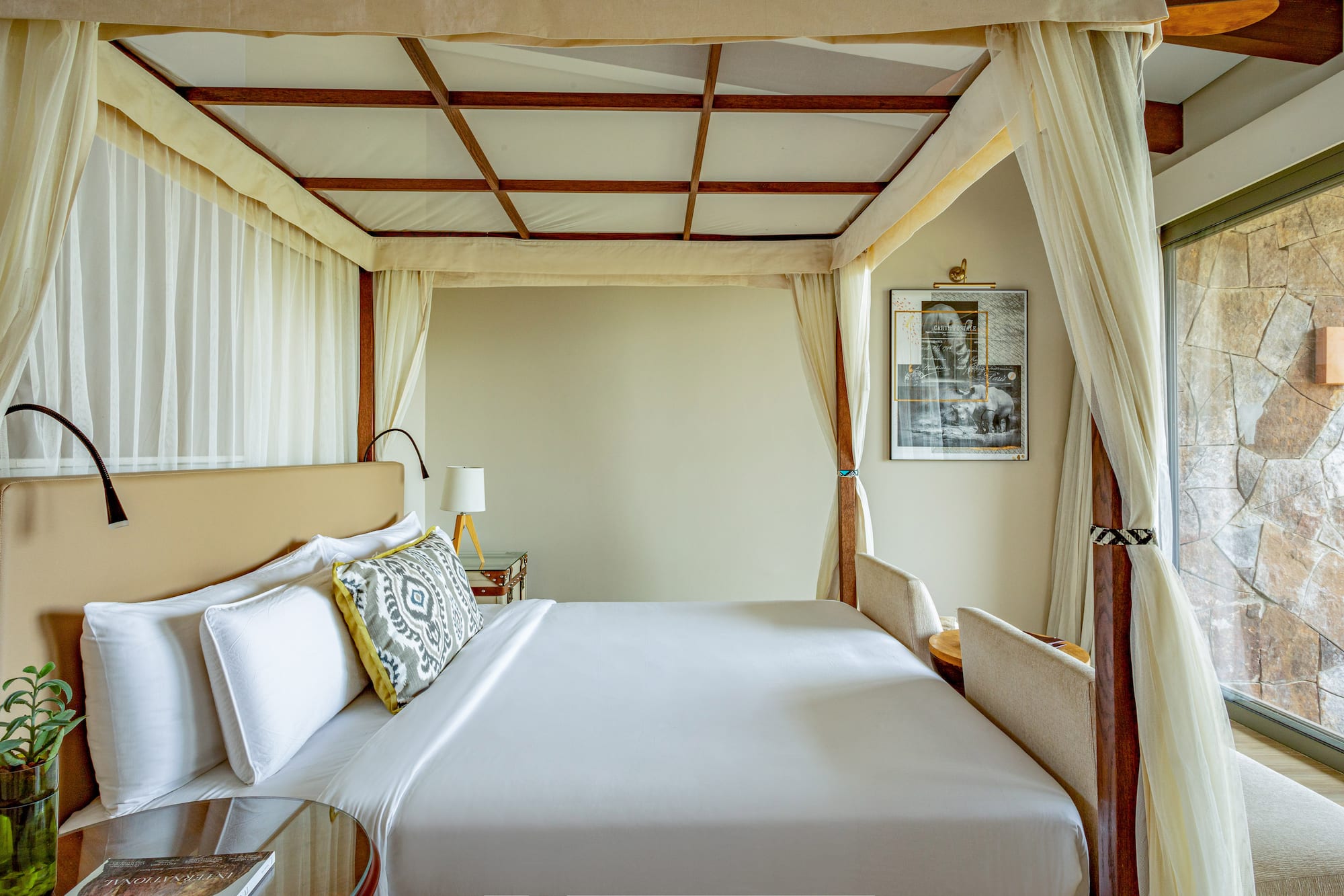 Luxury four-poster canopy bed with white linens in an elegant hotel room.