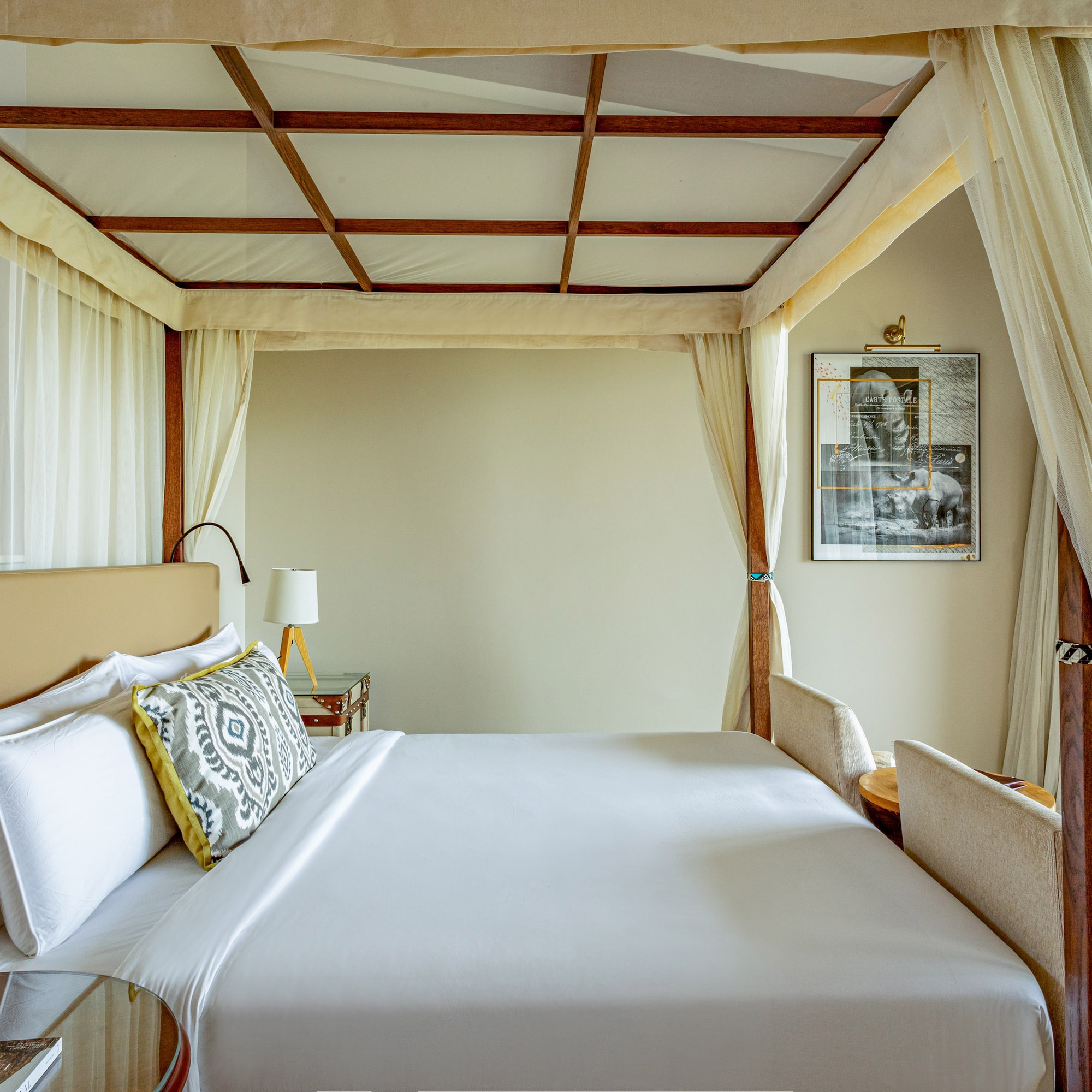 Luxury four-poster canopy bed with white linens in an elegant hotel room.