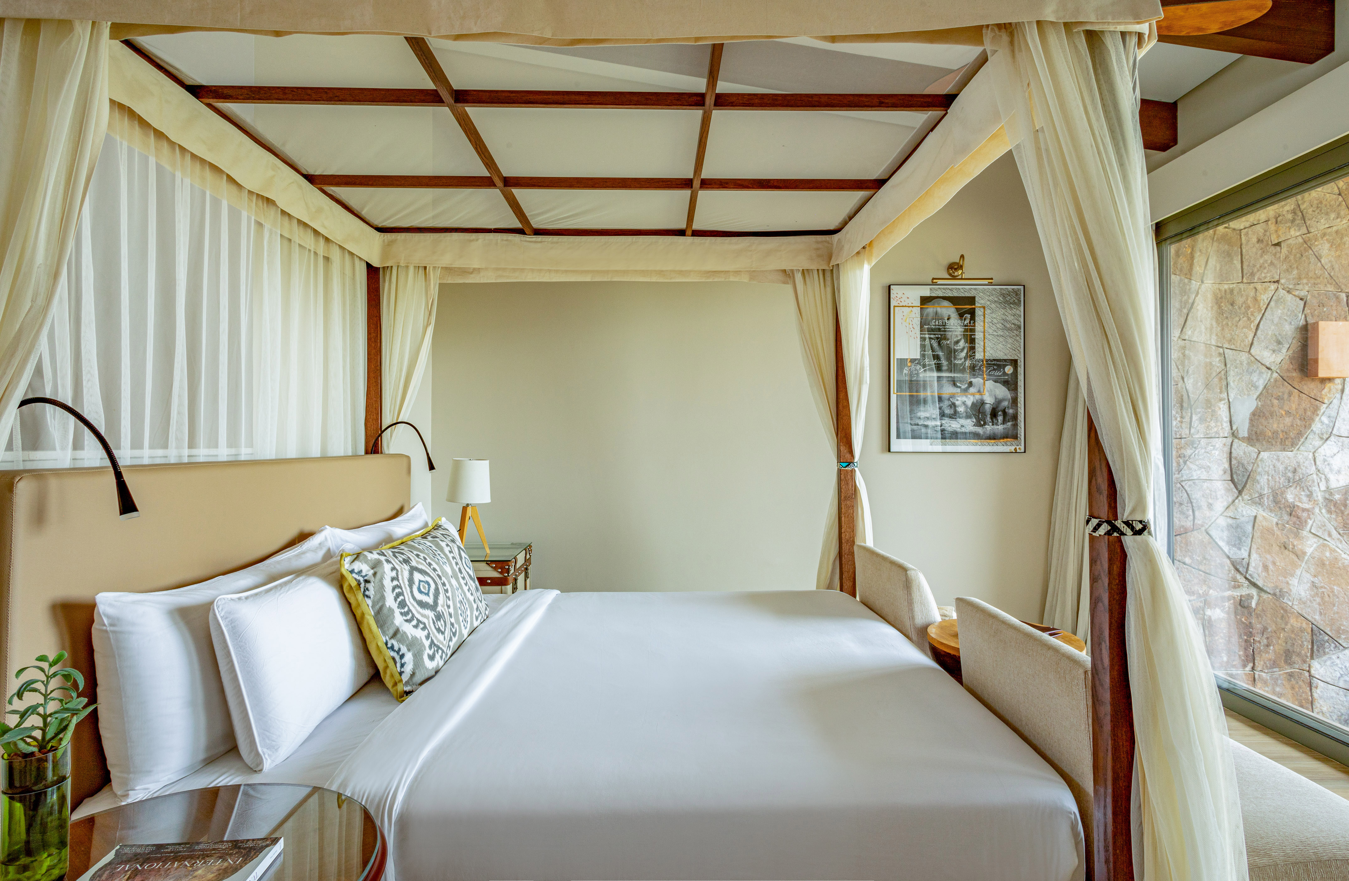 Luxury four-poster canopy bed with white linens in an elegant hotel room.