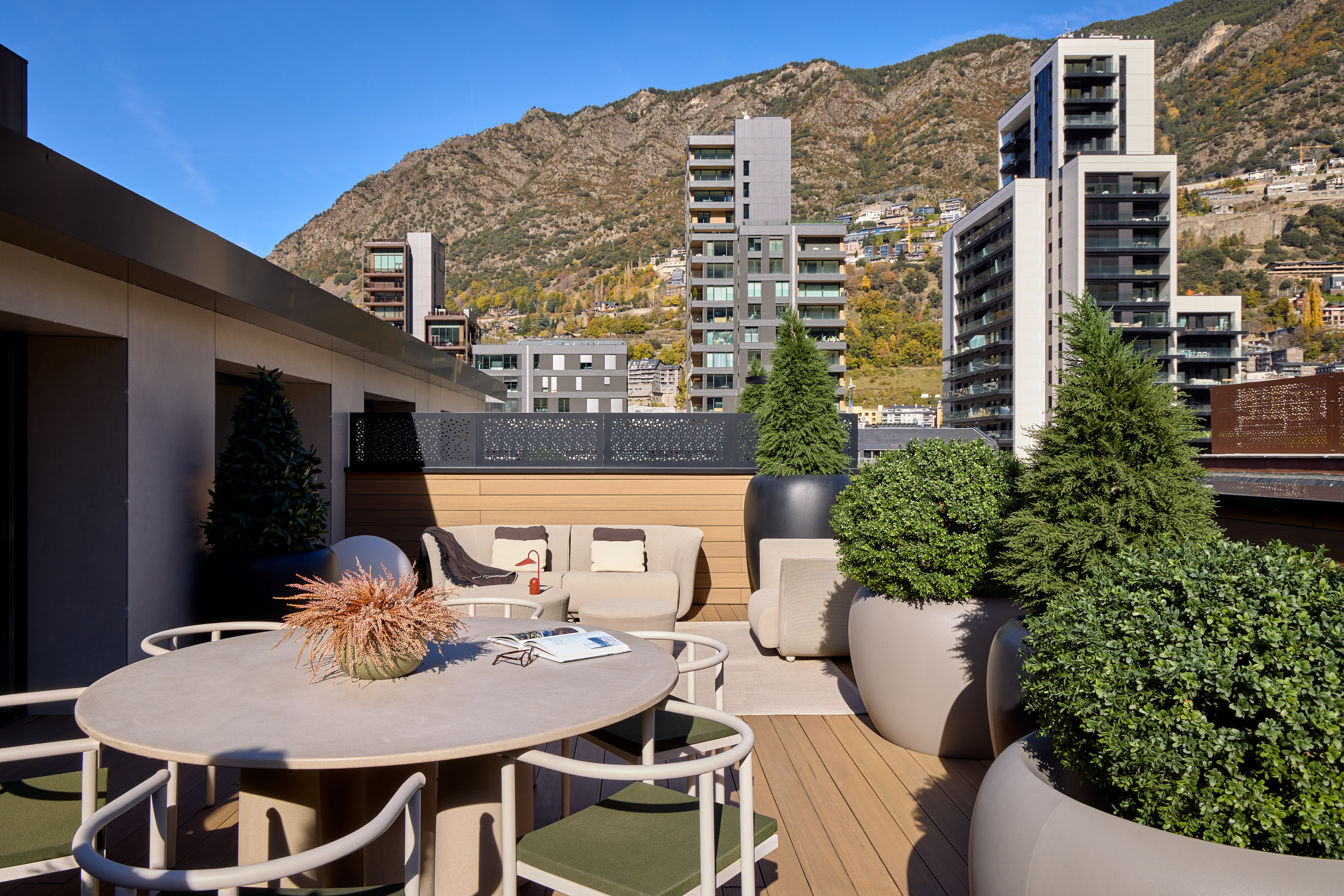 Modern urban rooftop terrace with outdoor seating, lush plants, and mountain views.
