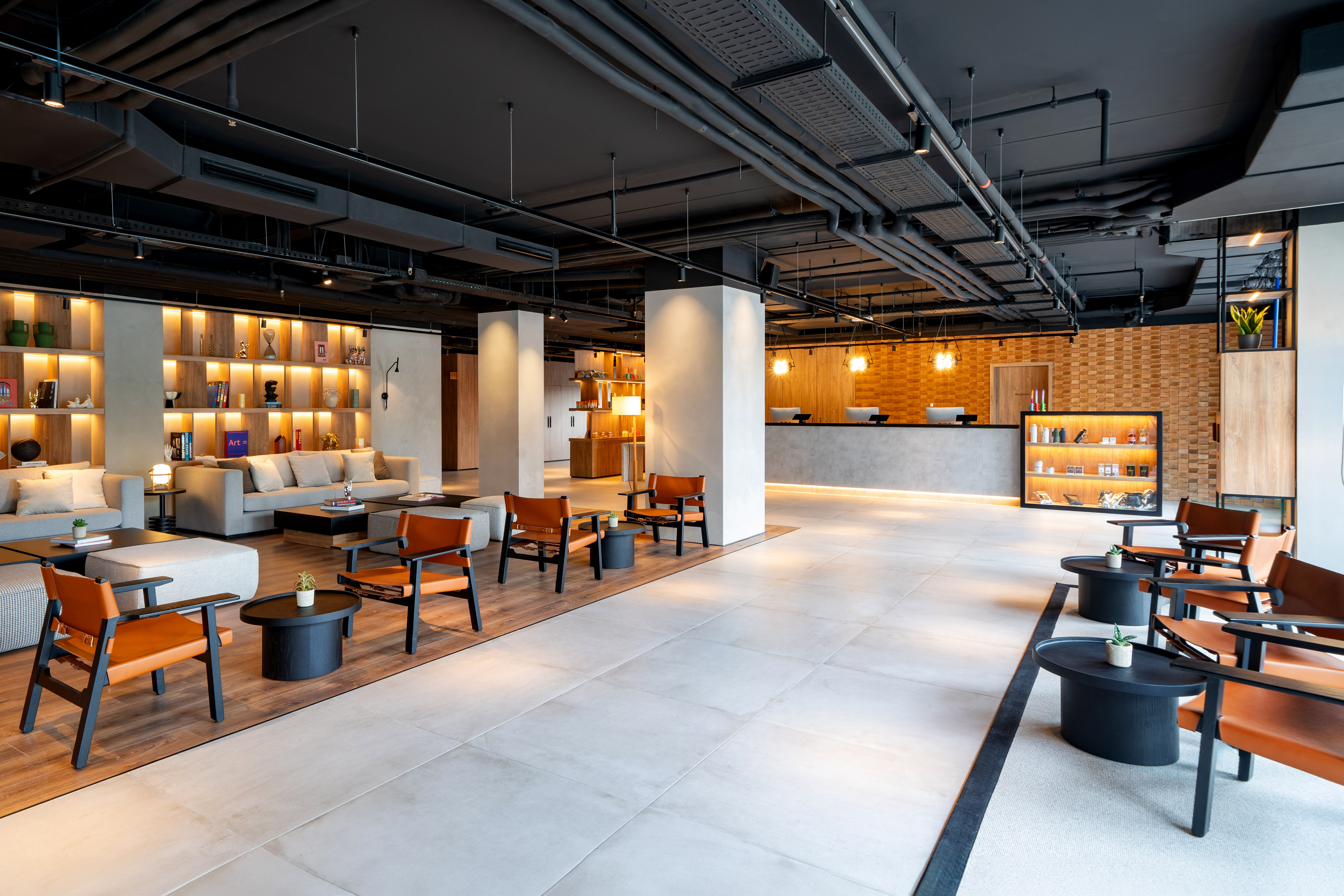 Modern hotel lobby interior with reception, lounge seating, and industrial ceiling.